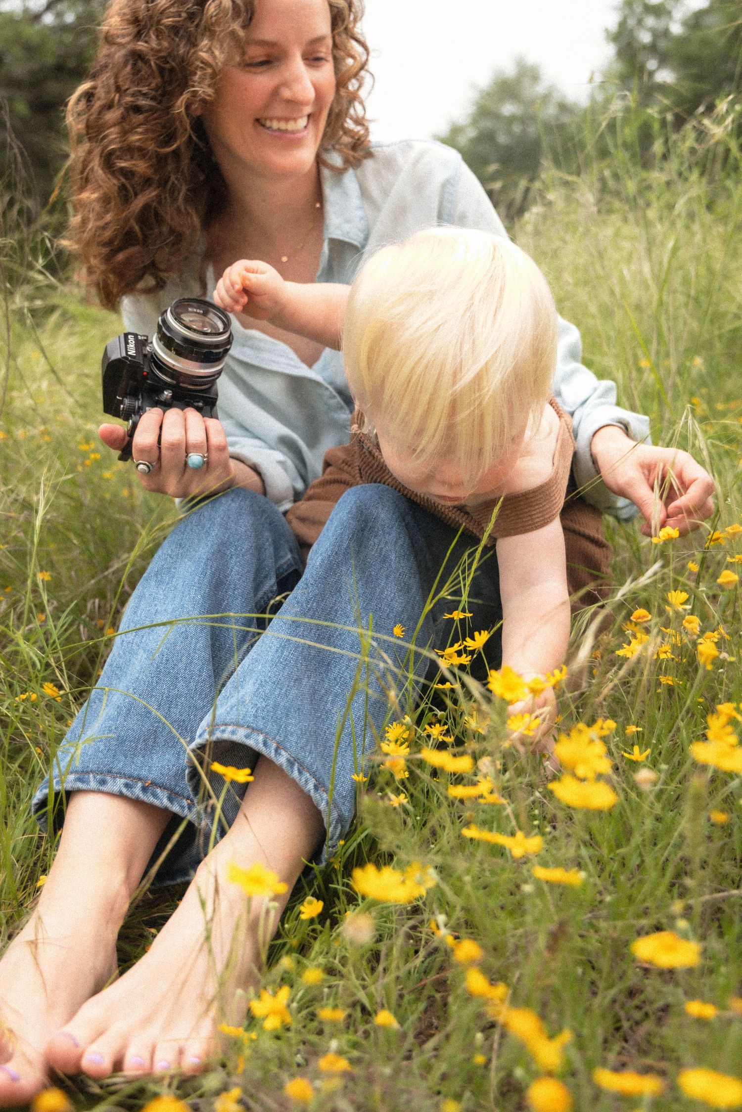 Photographer holds camera and toddler on lap in field of yellow wildflowers | Maddy Wilson, Wandering Wilsons Photography
