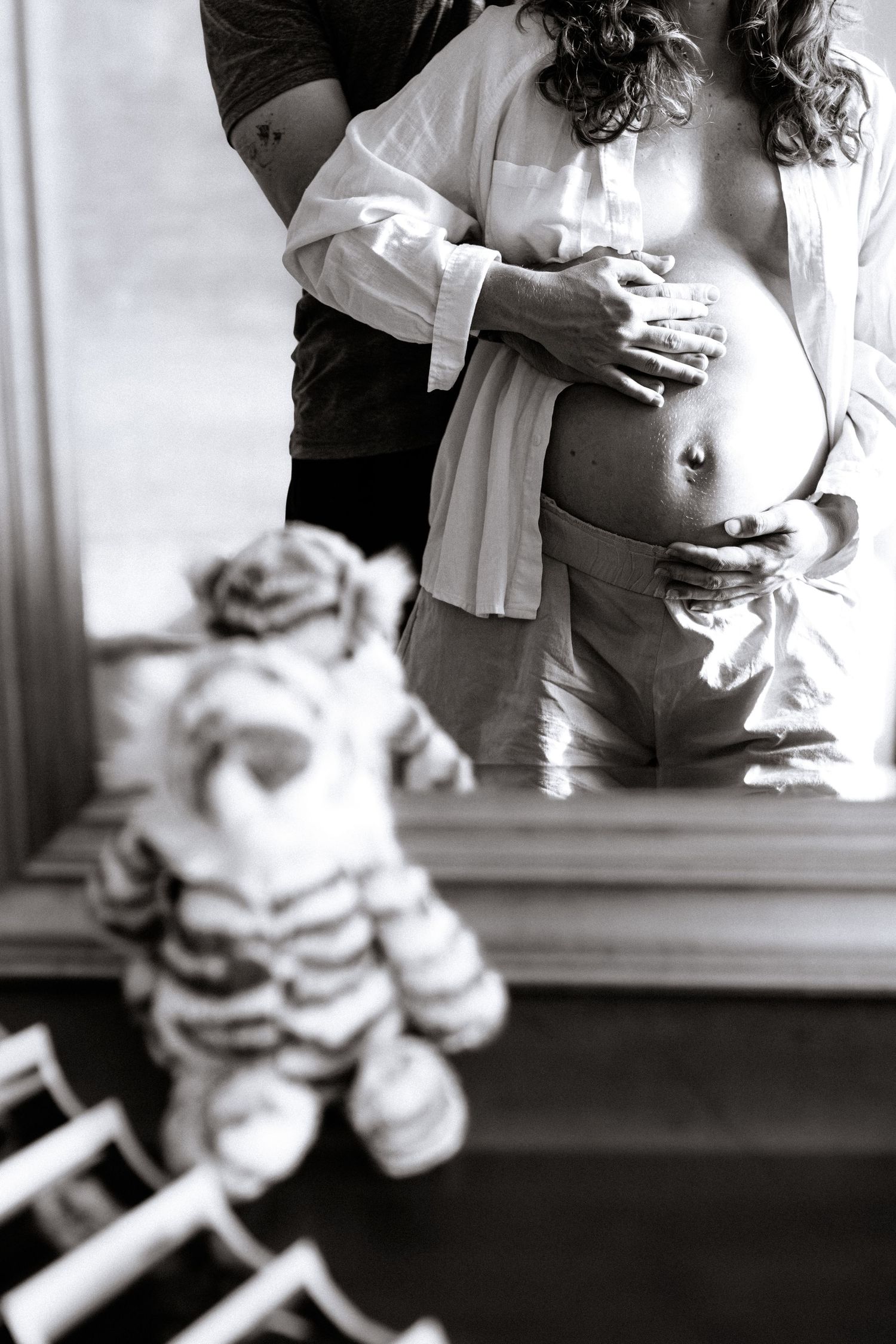 Couple touching baby bump in mirror with sonogram and tiger Jellycat during at-home maternity session