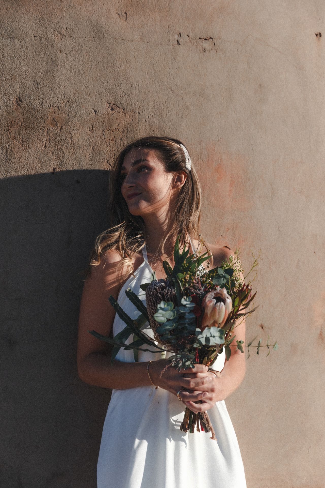 Bride holds her bouquet against wall with artistic shadows before beach elopement