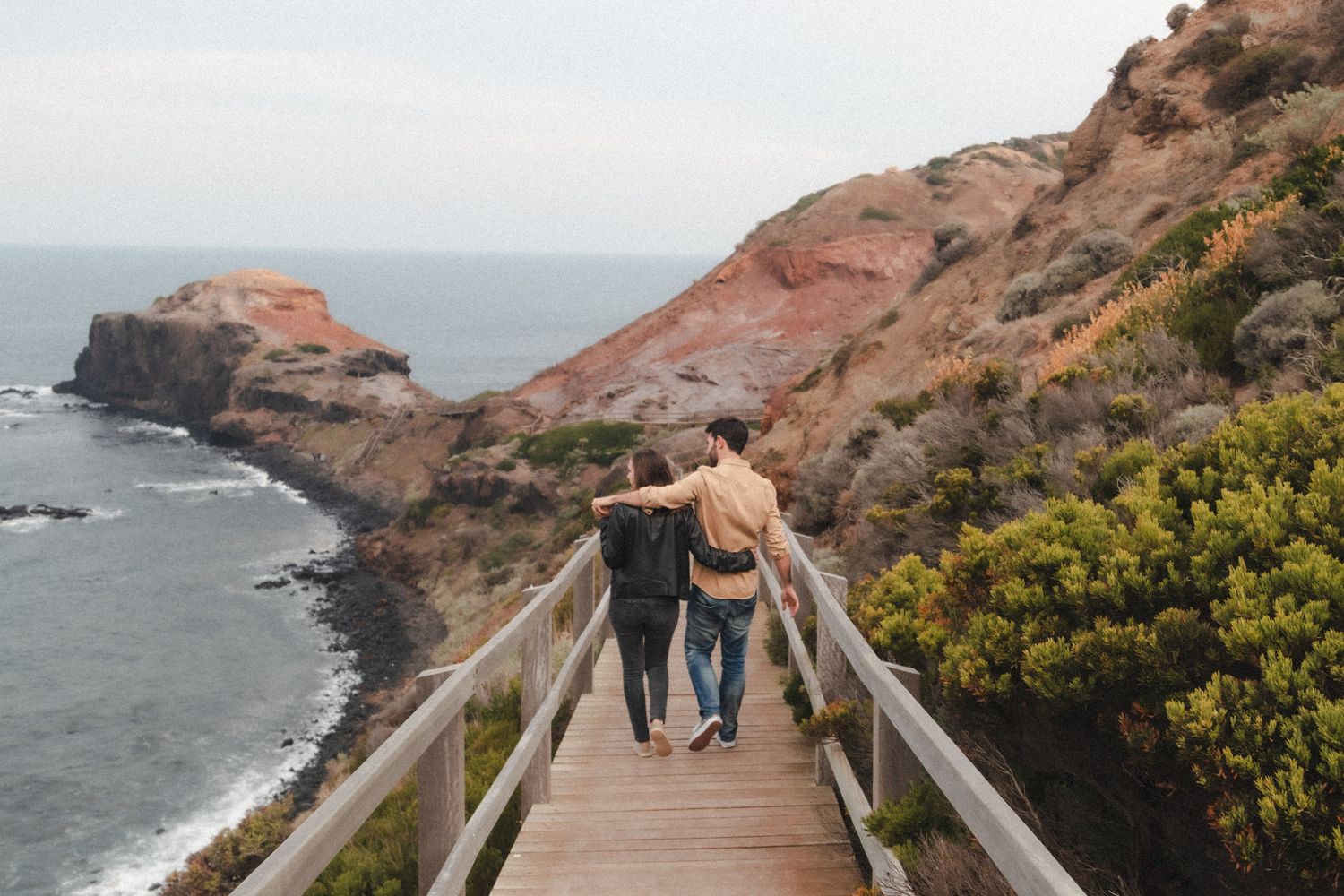 Couple walking arm in arm down boardwalk during coastal engagement session