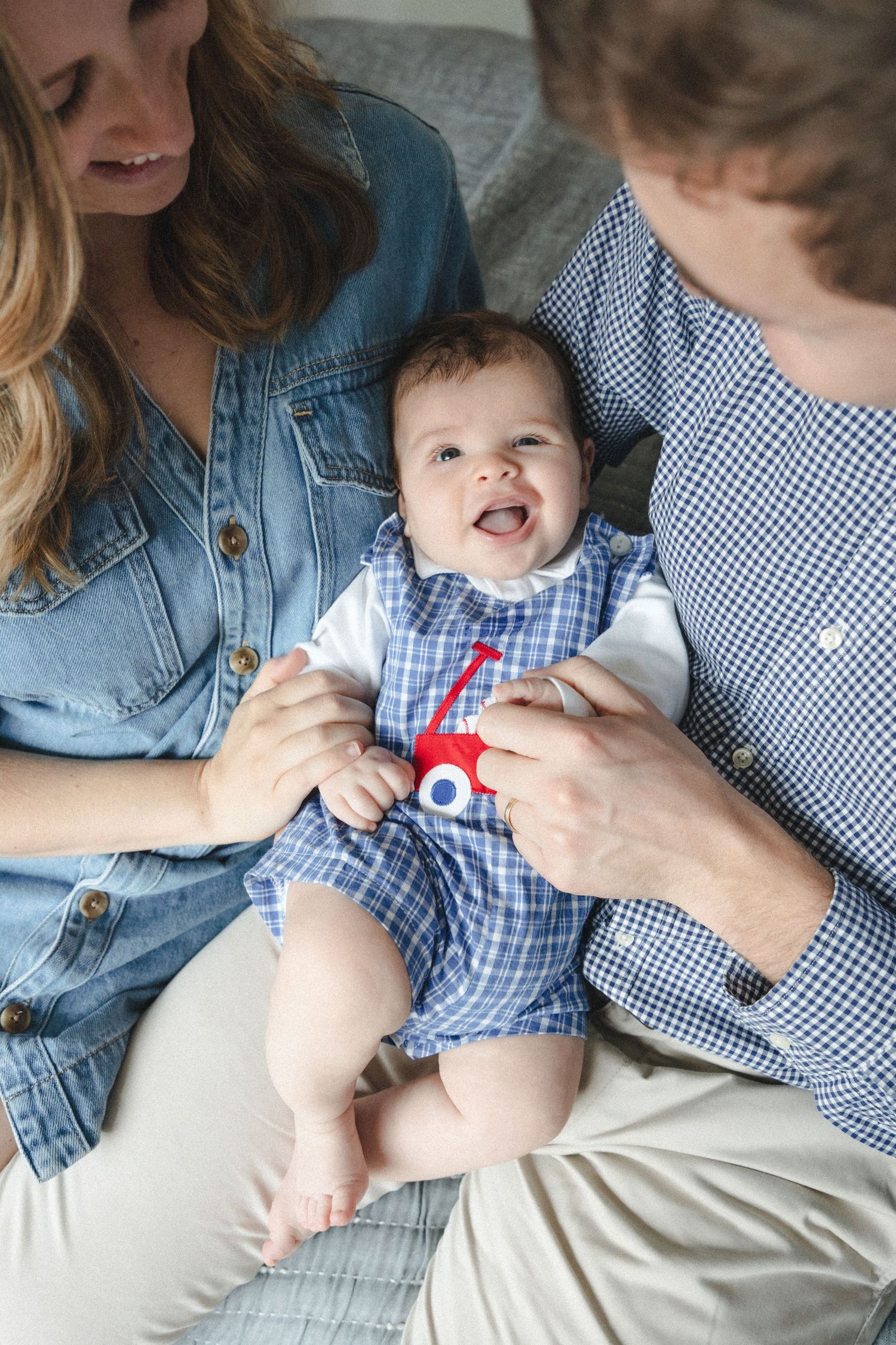 Couple cuddles laughing young infant during in-home family photography session