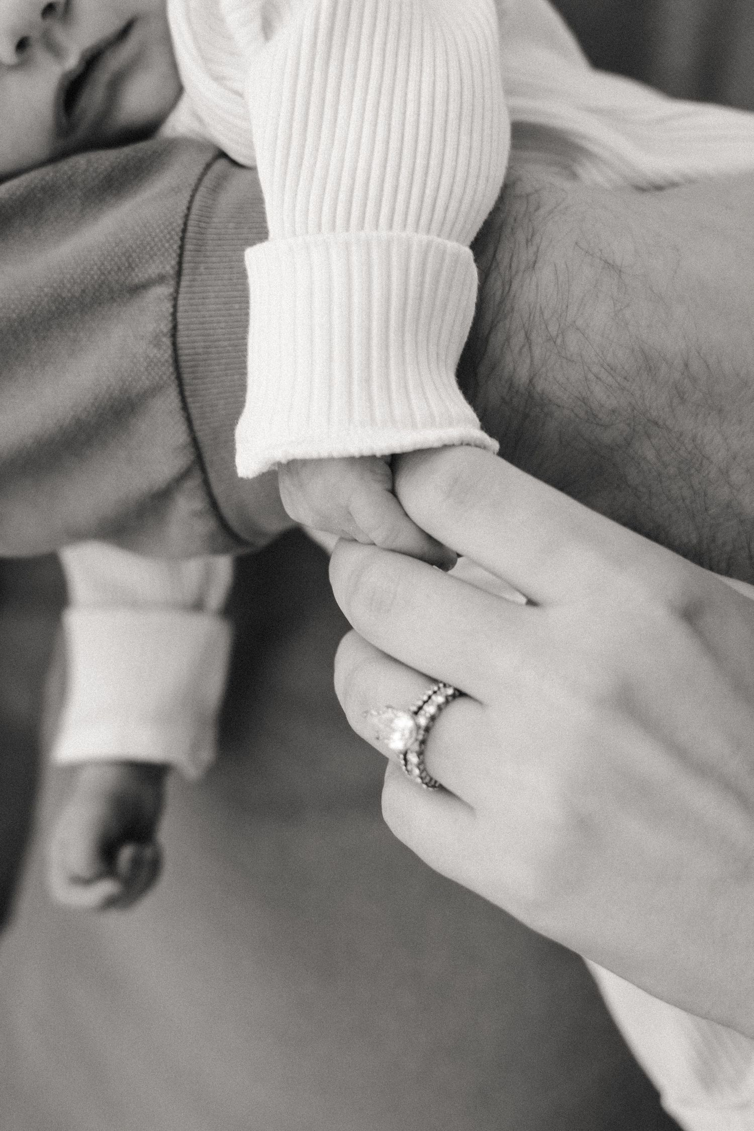Mom holds newborn baby's finger in dad's arms during at-home newborn photography session