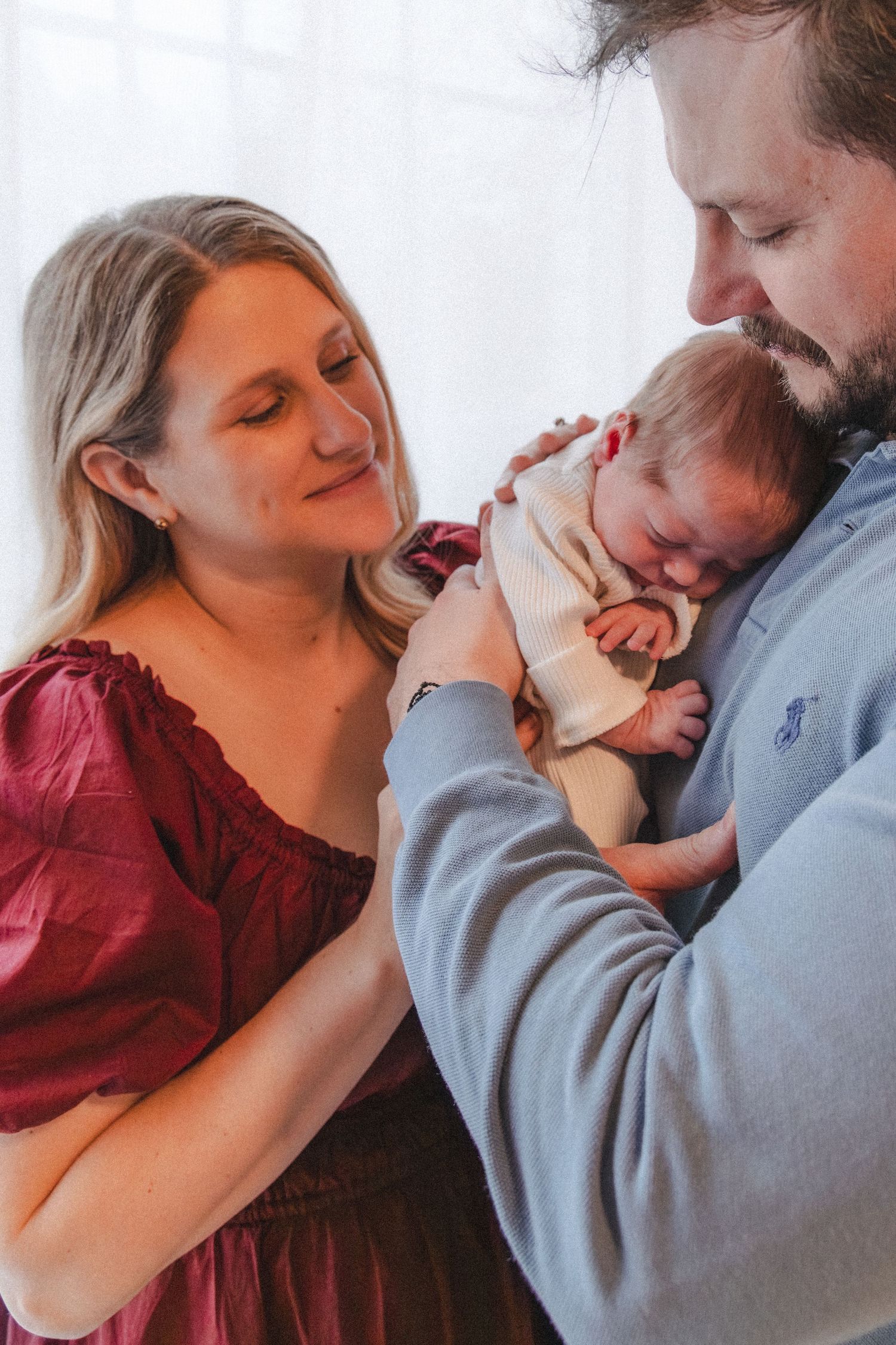 Couple cuddles newborn near paned window