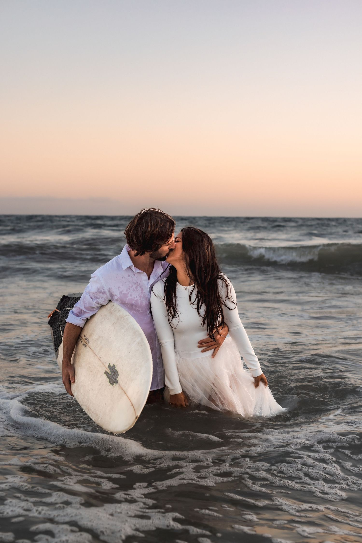 surfing couple kiss during trash the dress beach session