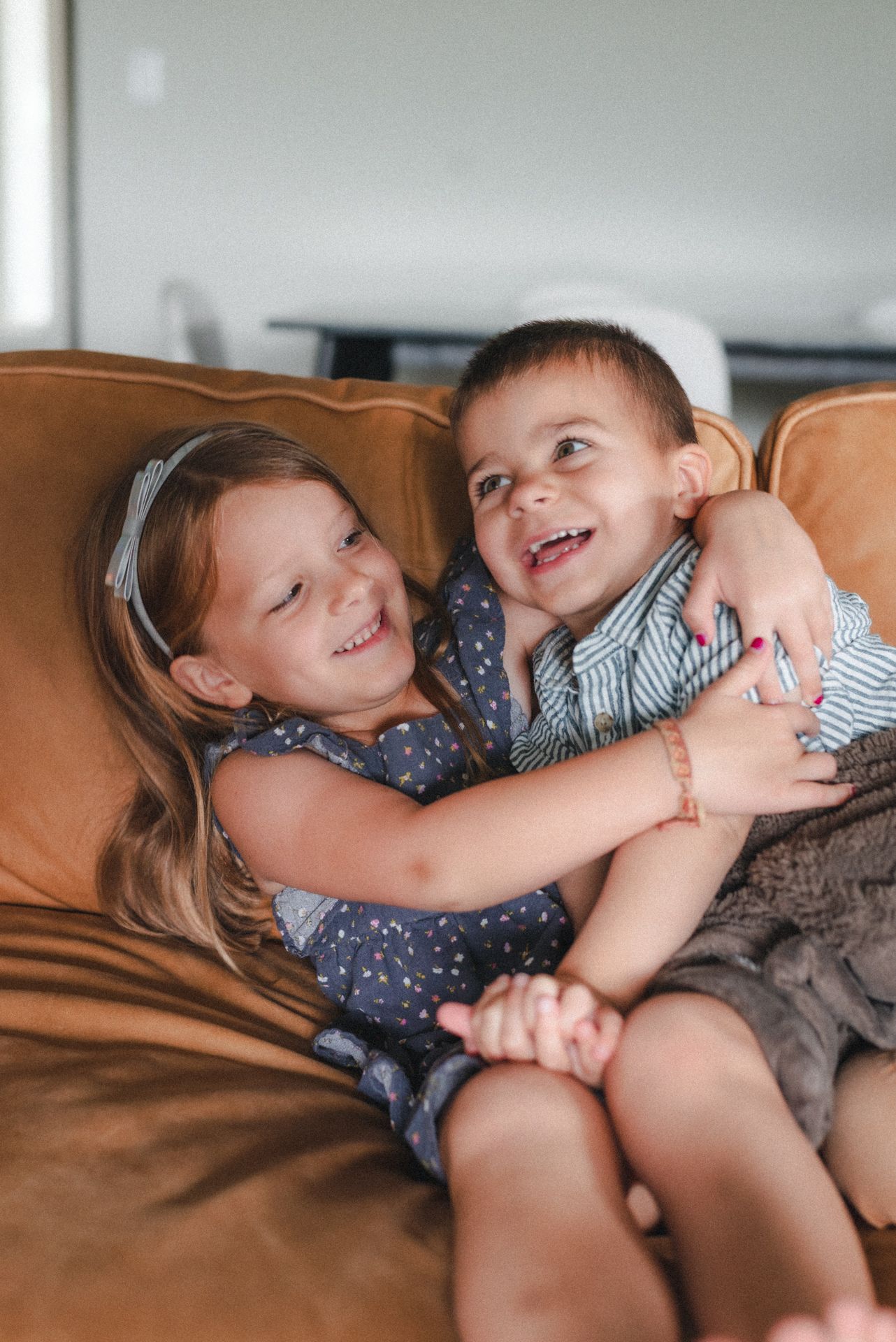 Siblings embracing and laughing on couch during at-home family session