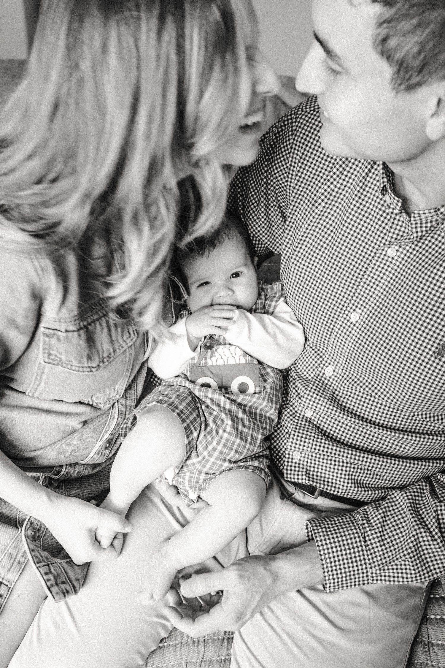 Mom and dad go in for a kiss with infant on their lap during family photography session