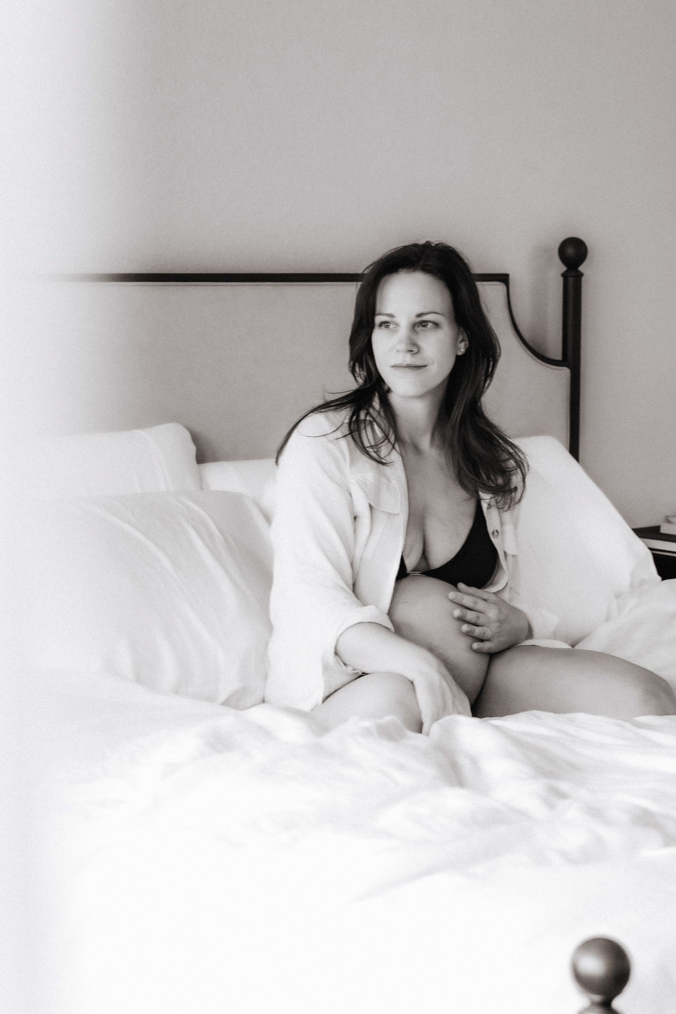 Pregnant woman holds belly and looks out window in brightly lit bedroom