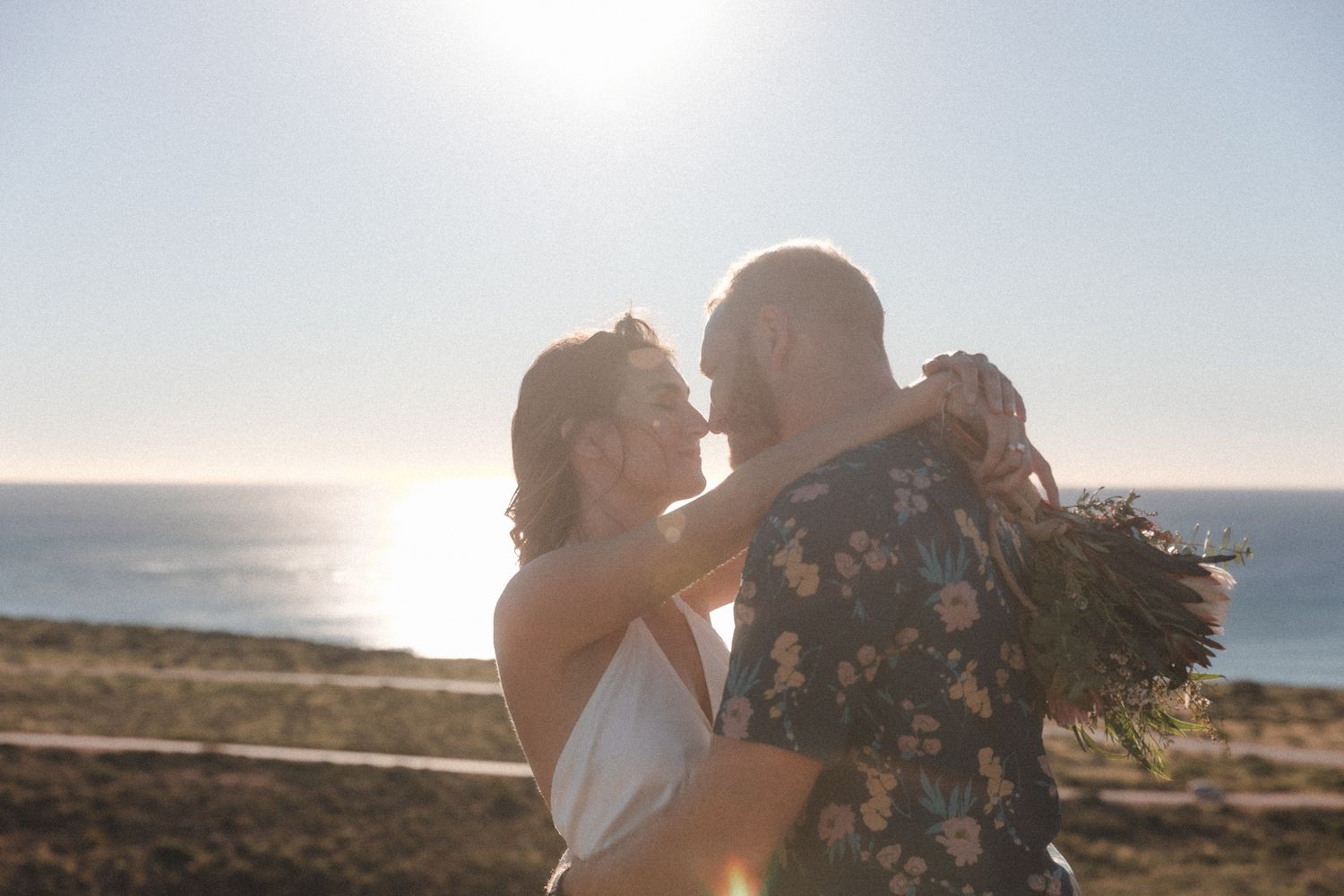 Couple hugs on cliffs above the ocean during beach elopement ceremony