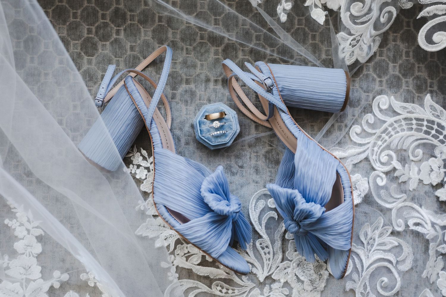 Bride's details - blue wedding shoes, wedding rings, and lace veil flat lay