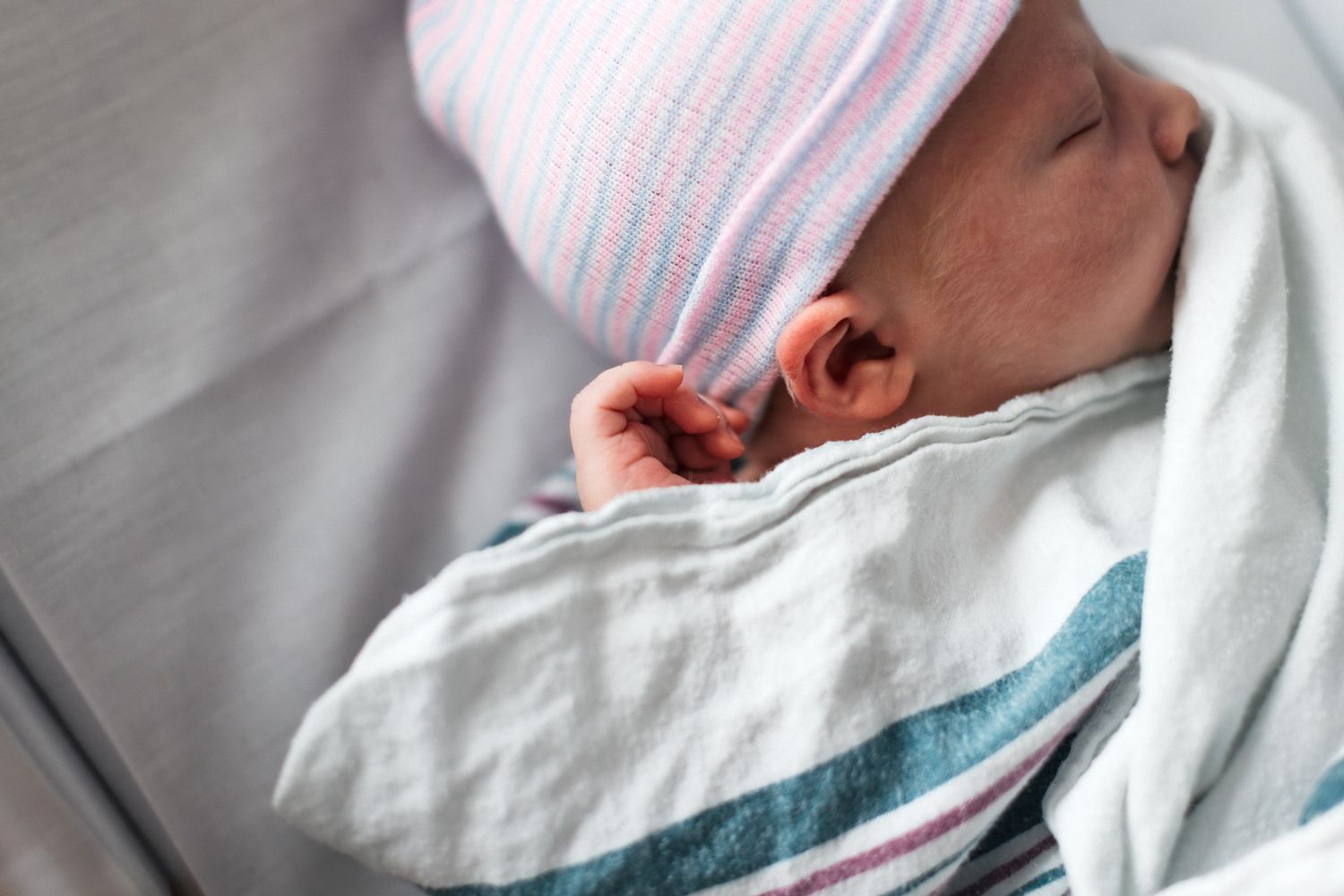 Newborn baby snuggles in blanket and hospital hat right after hospital birth during Fresh 48 newborn photography session