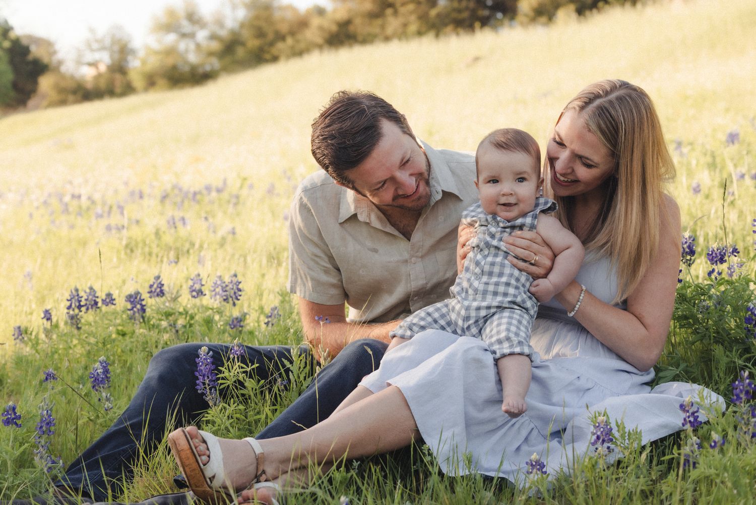 Parents hold infant in the bluebonnet fields at sunrise in the Texas Hill Country.