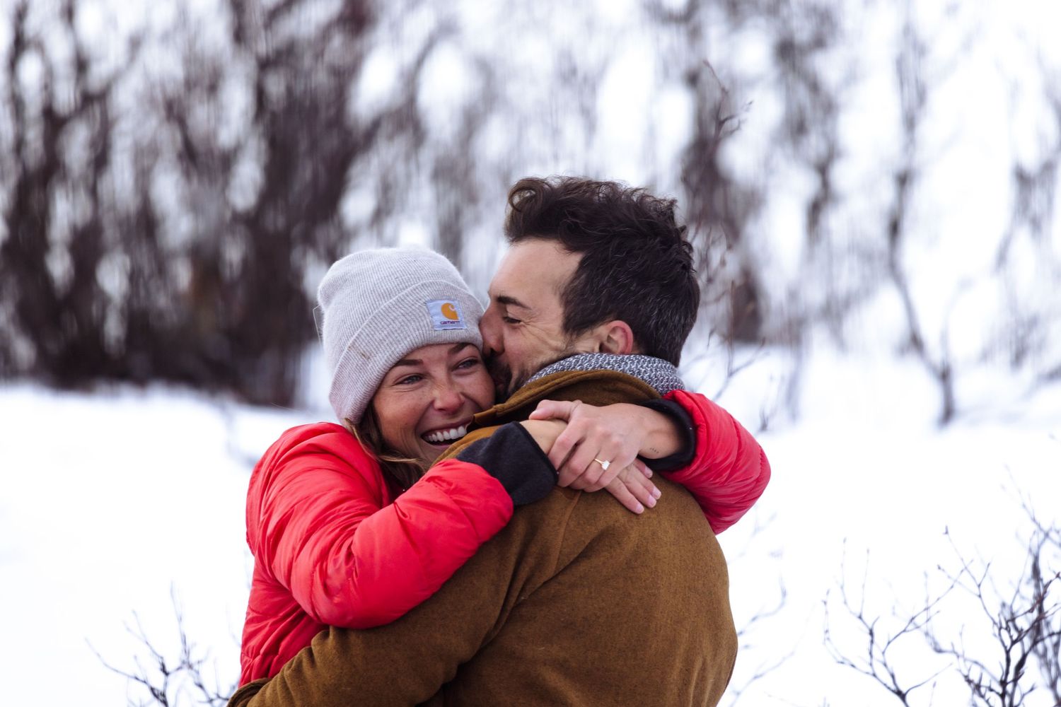 Woman in red jacket hugging her new fiancé after their engagement in Arctic Sweden.
