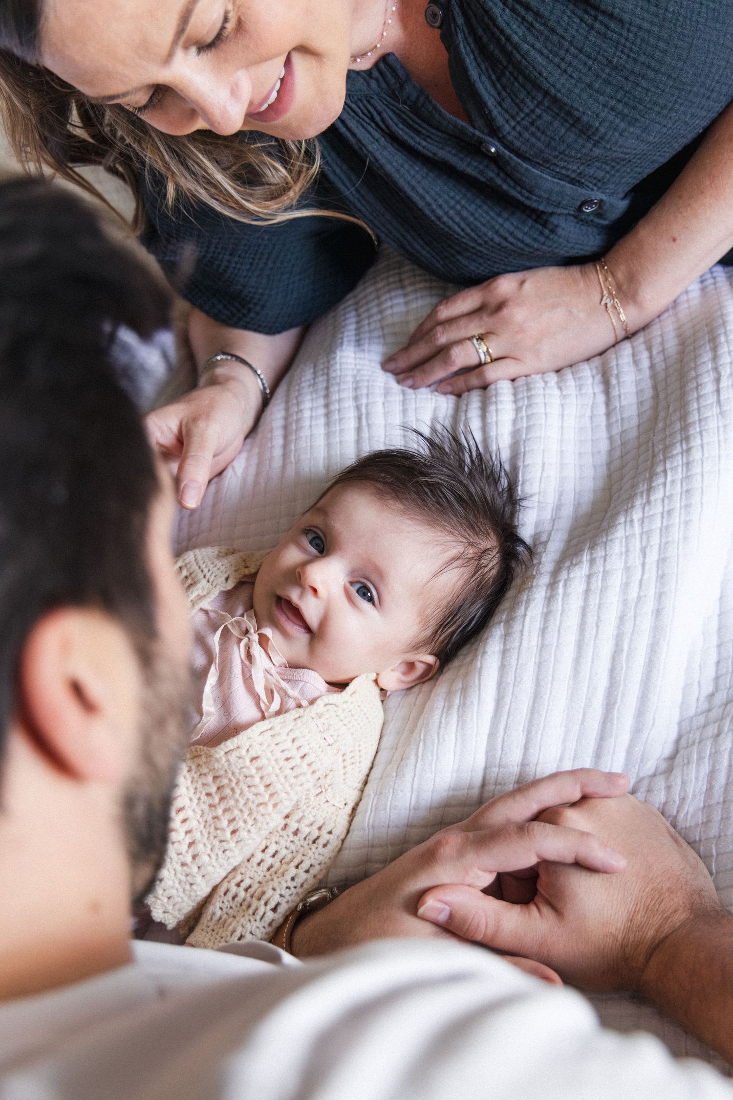 Baby smiling at camera on bed between parents at home in Austin, Texas