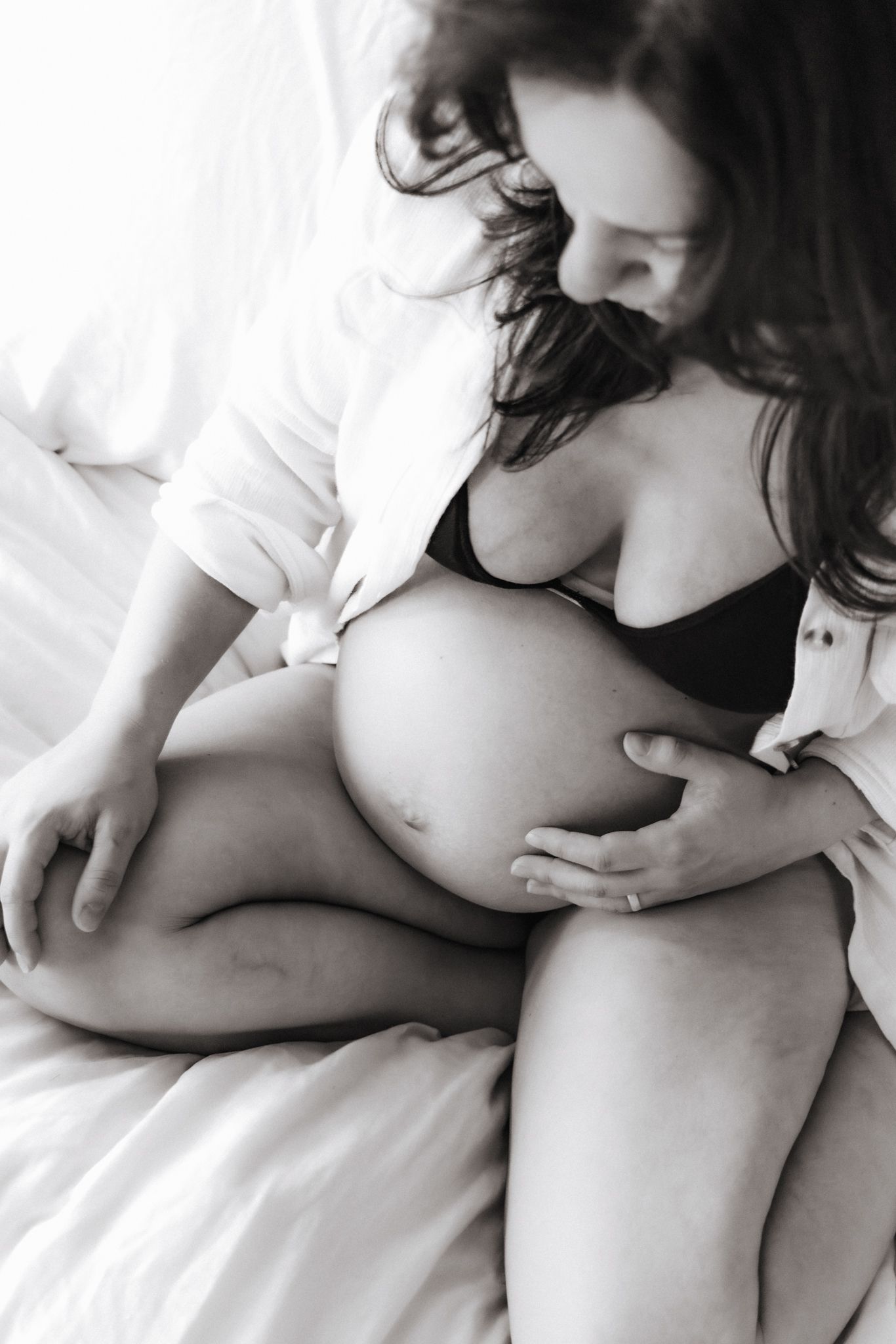 Pregnant woman in black bra holds belly during maternity session