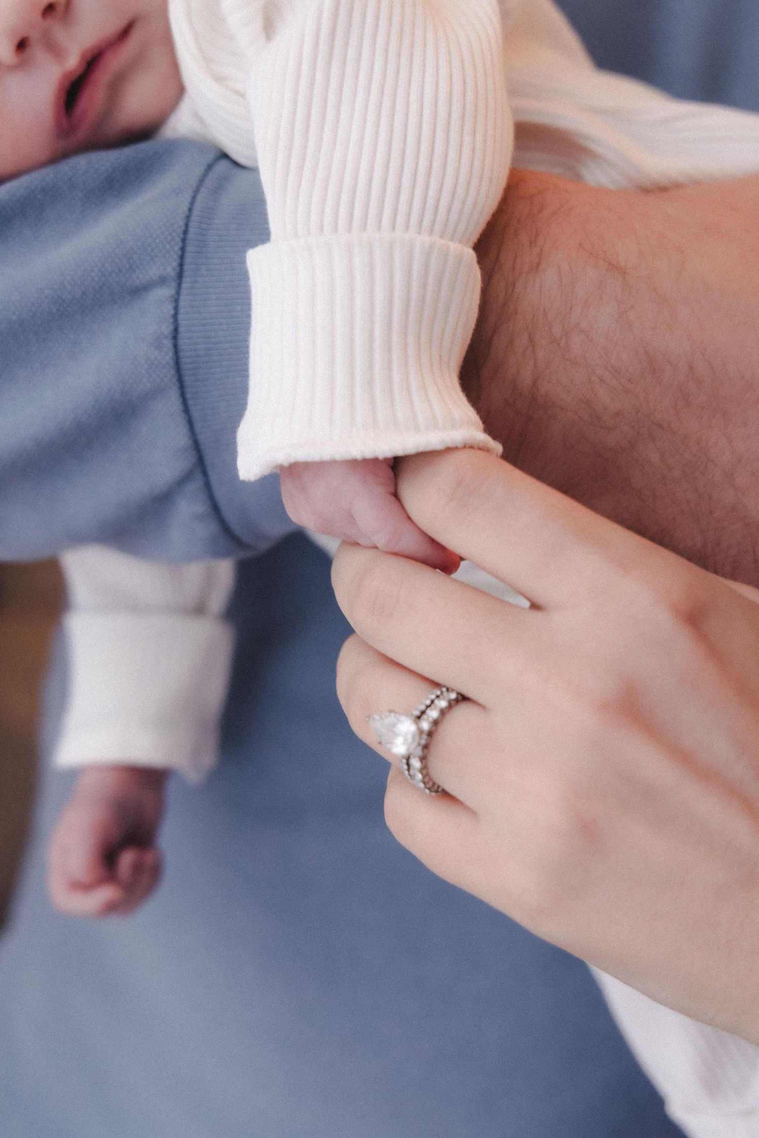 Mother with her wedding rings holds her newborn baby's hand while father holds the baby in his arms.