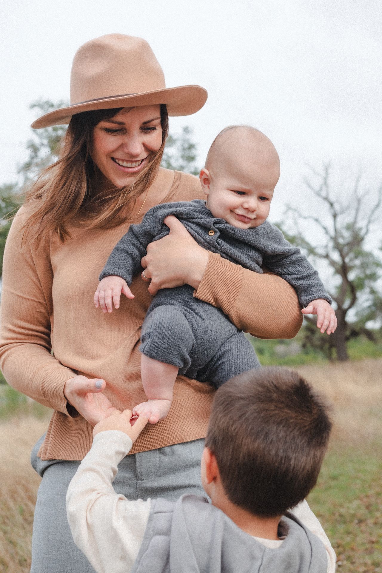 Mom holds infant while brother plays with his feet during during a ranch family photo session