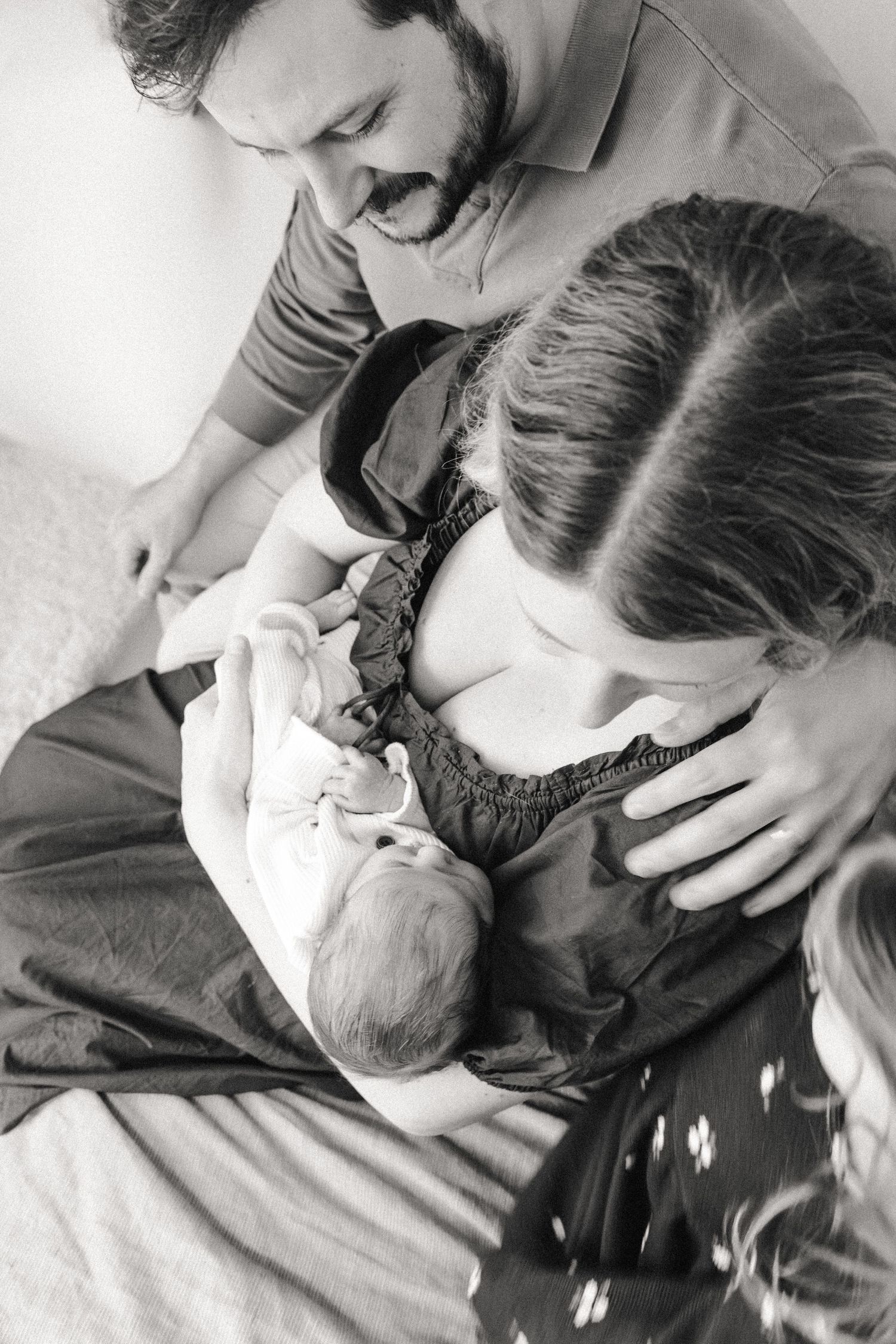 Family cuddles around mom and newborn baby during at-home newborn session