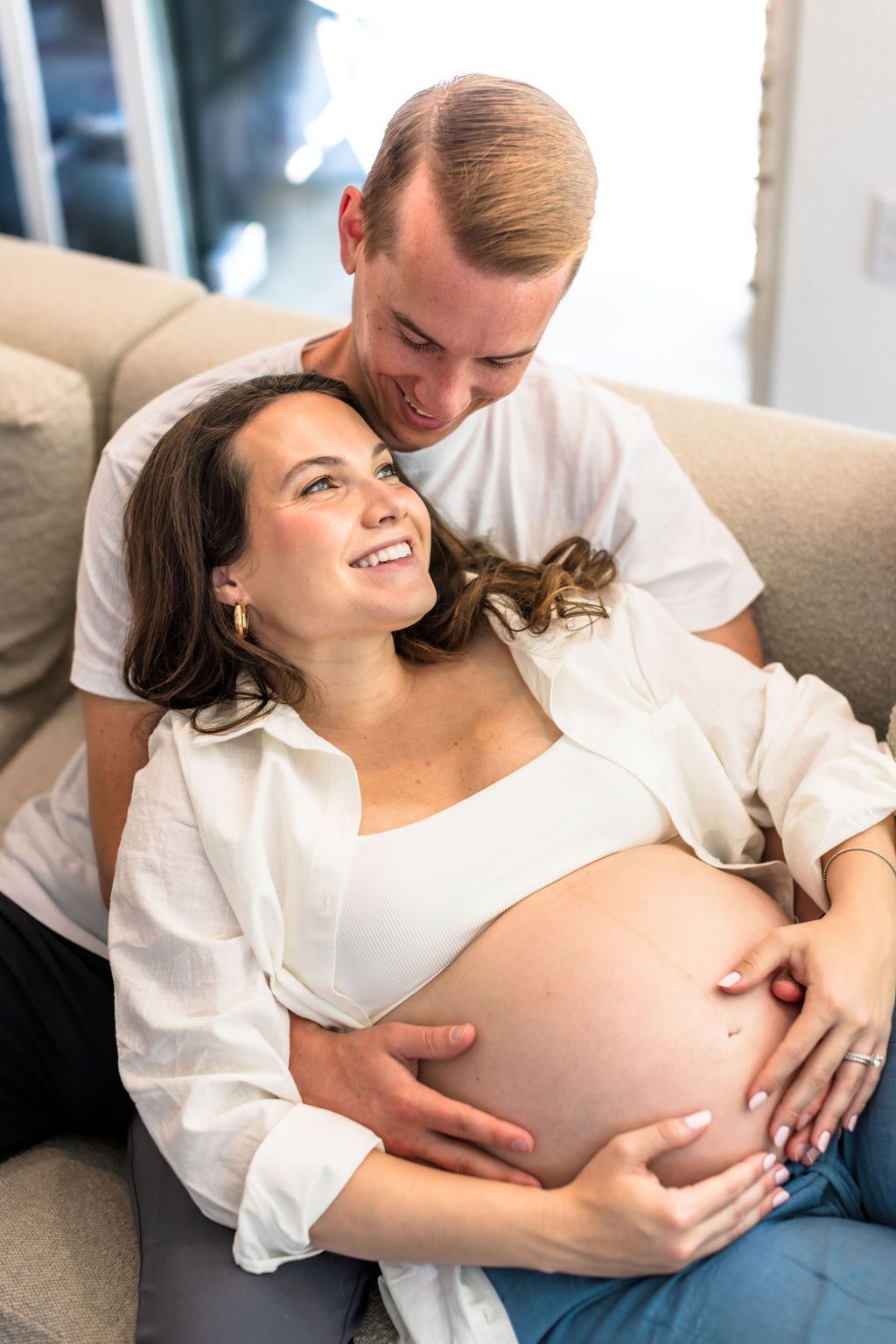 Beautiful couple cuddles on couch during at-home maternity session | 37 weeks pregnant
