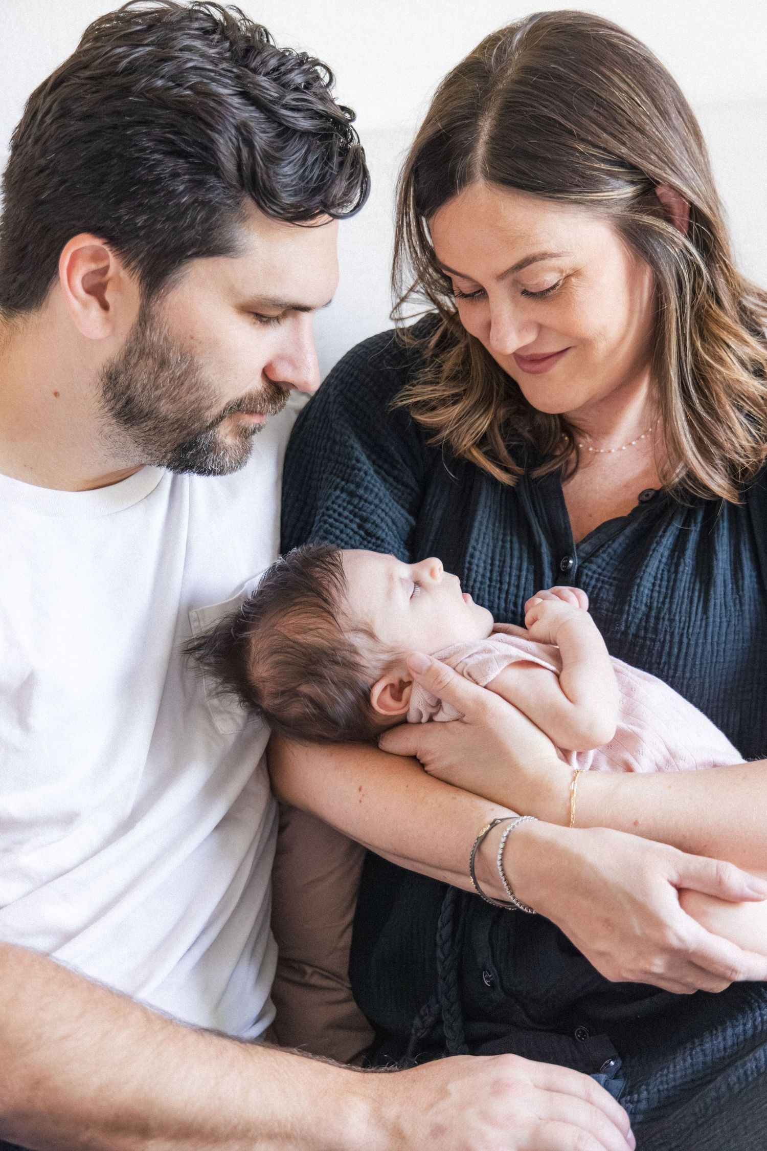 Father and mother holding new baby in their arms while sitting on bed