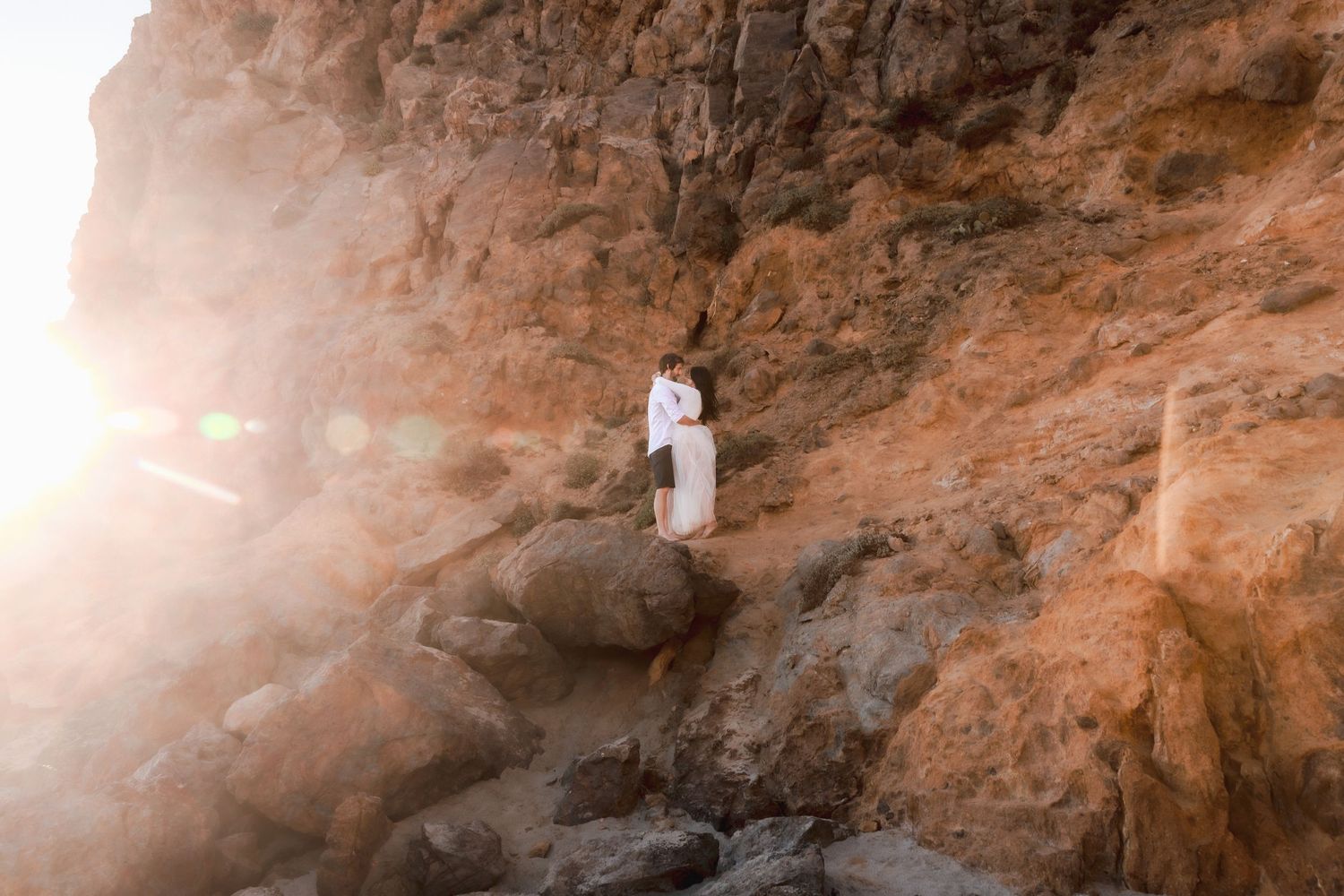 Couple embraces at sunset on red rocks with sun flare |  Elopement photography session