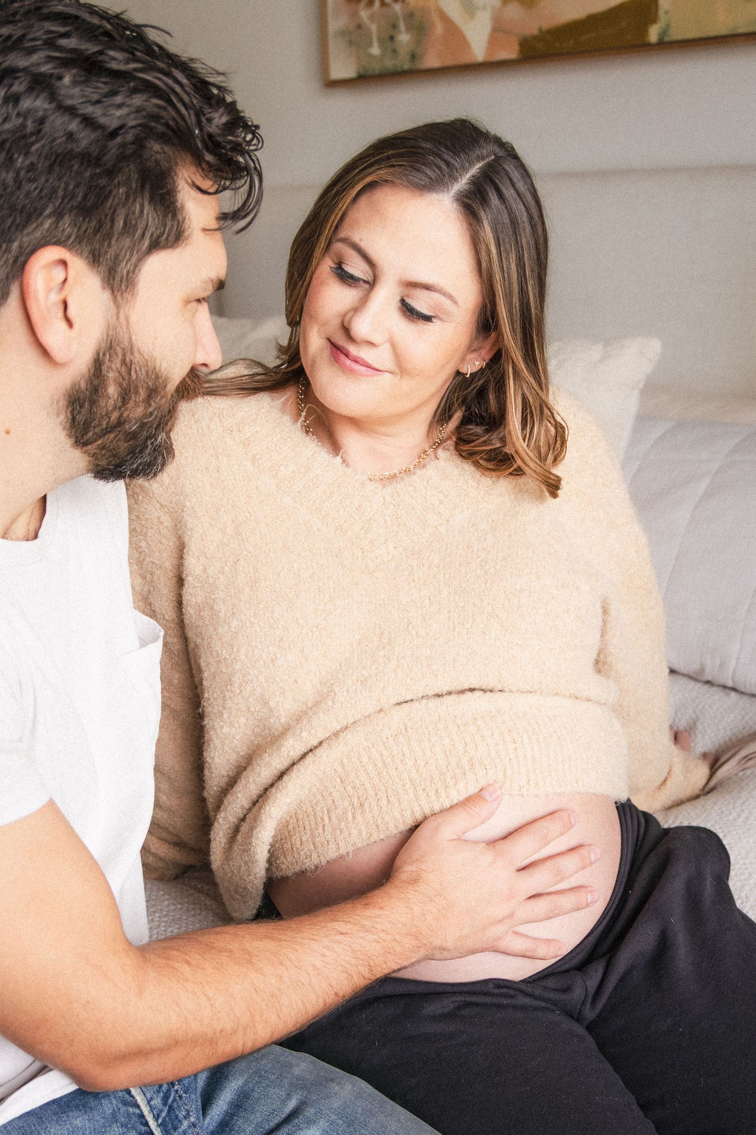 Husband places hand on pregnant wife's baby bump during at-home maternity photography session