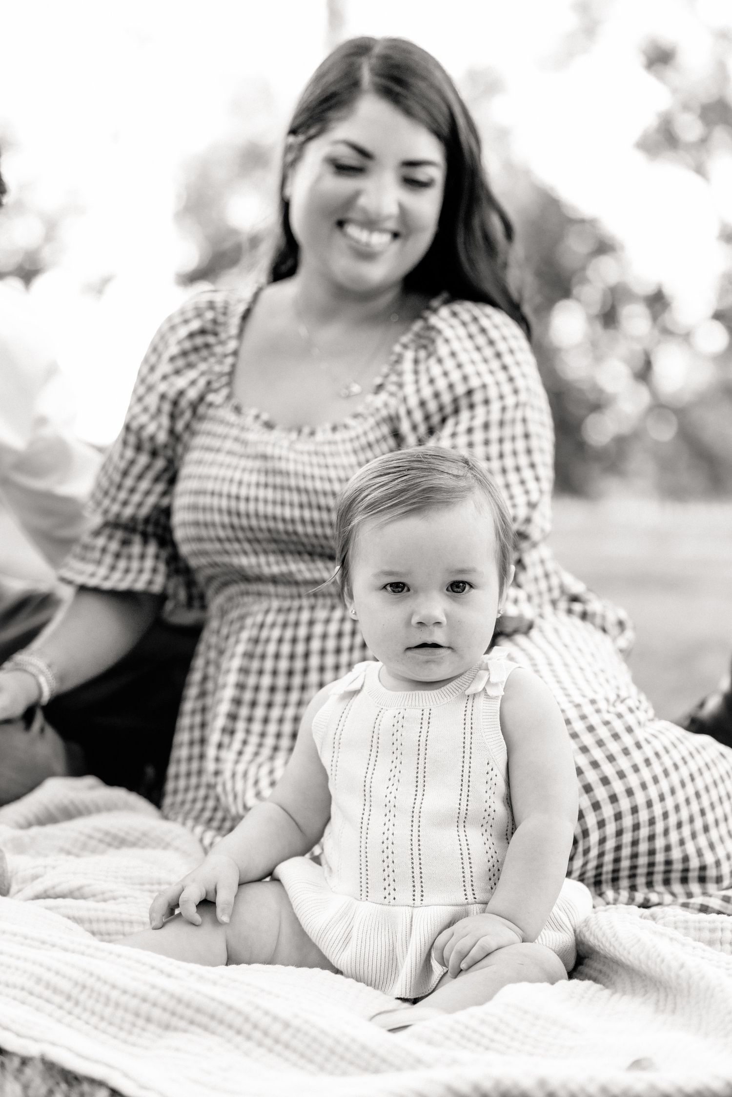 Mother smiling at young toddler on blanket during park family photography session