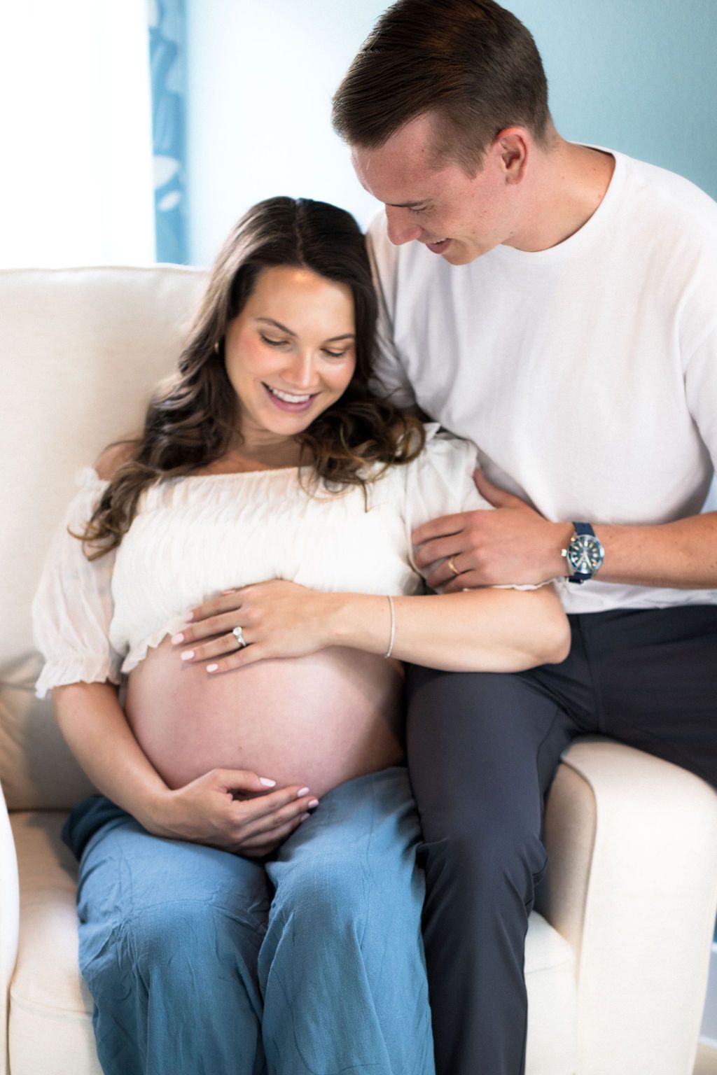 Couple in nursery chair looking at baby bump during at-home maternity session in Austin, Texas