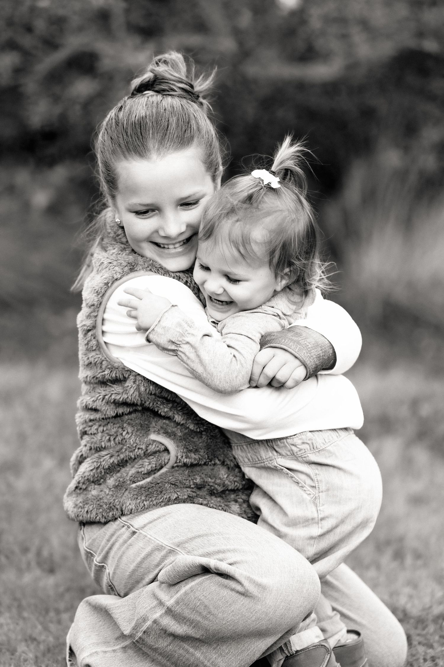 Girl siblings hug and play during outdoor family photography session