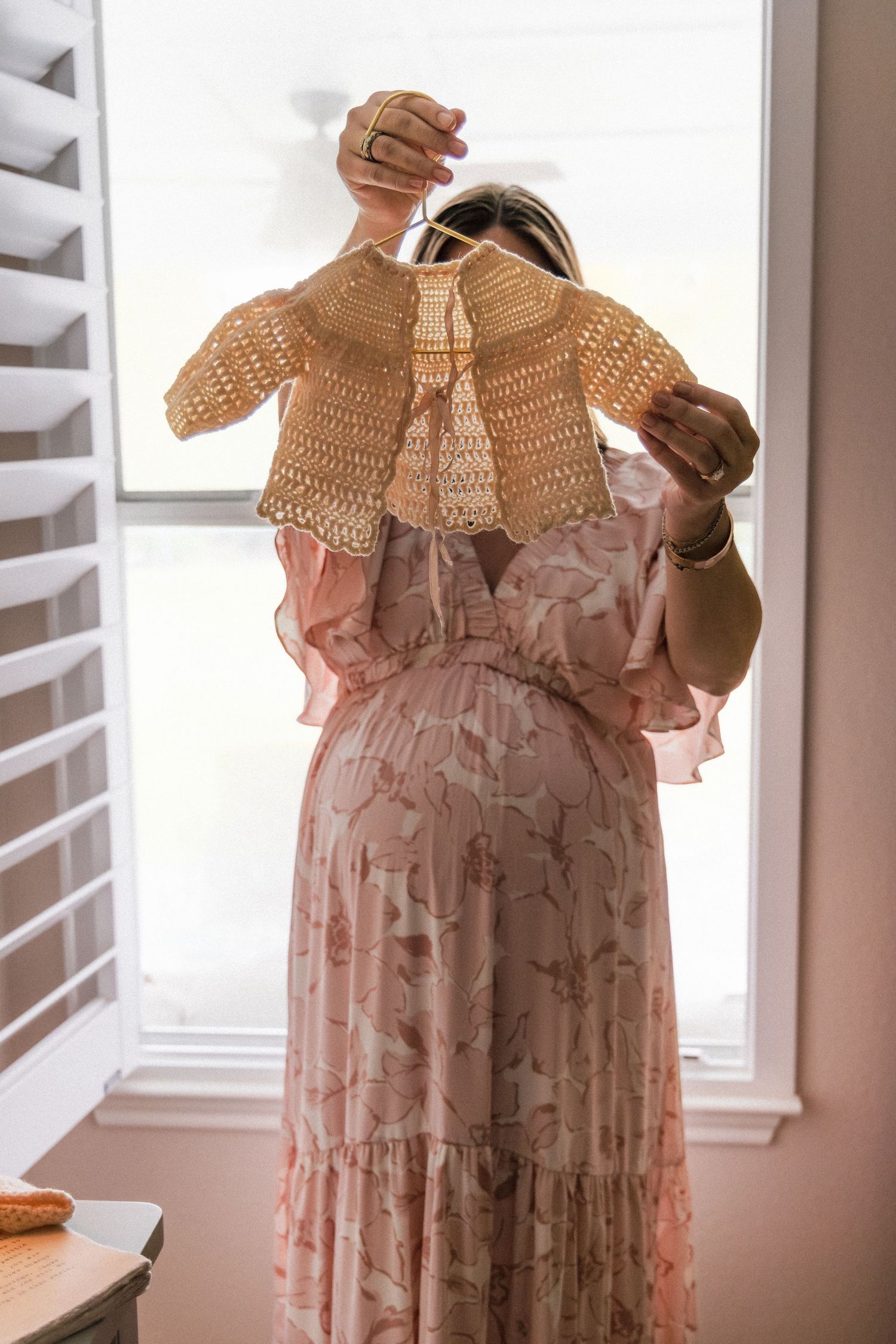 Mom holds up heirloom baby sweater at home during maternity photography session