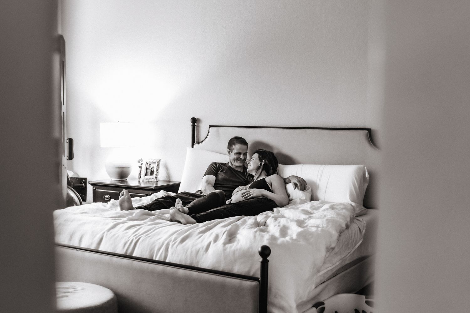 Husband and wife cuddling on bed during at-home maternity session