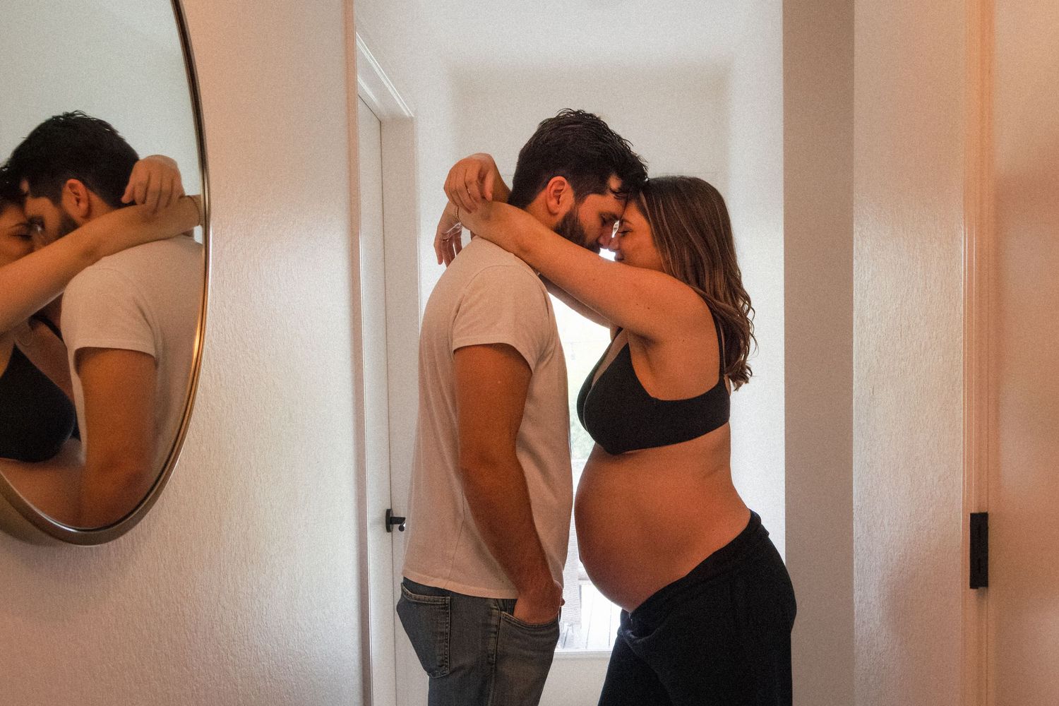 Pregnant woman hugs husband in hallway of their home in Austin, Texas