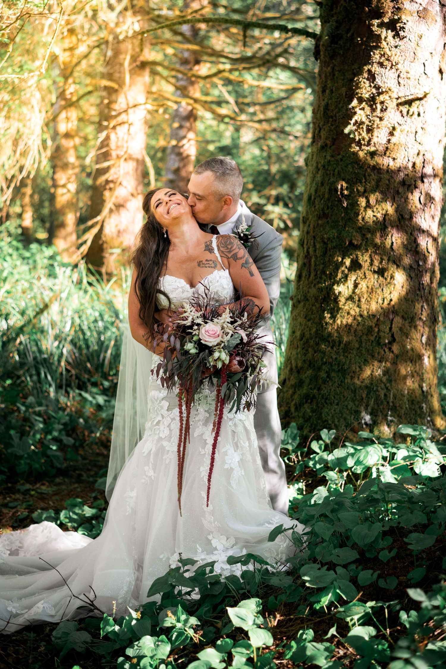 A romantic wedding photo of a couple with bouquet in a sunlit forest.