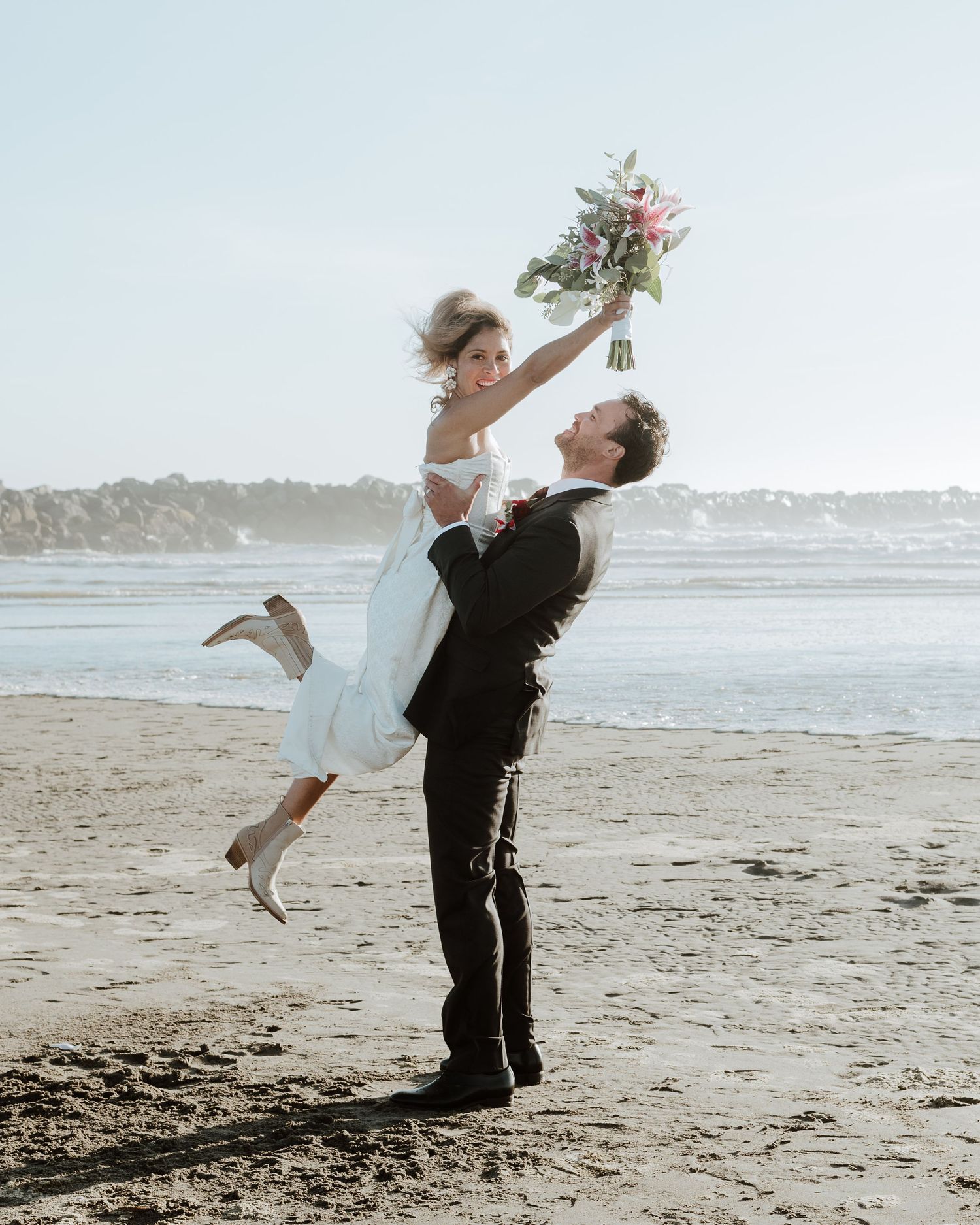 Joyful wedding couple celebrating with playful lifts on a sunny beach.