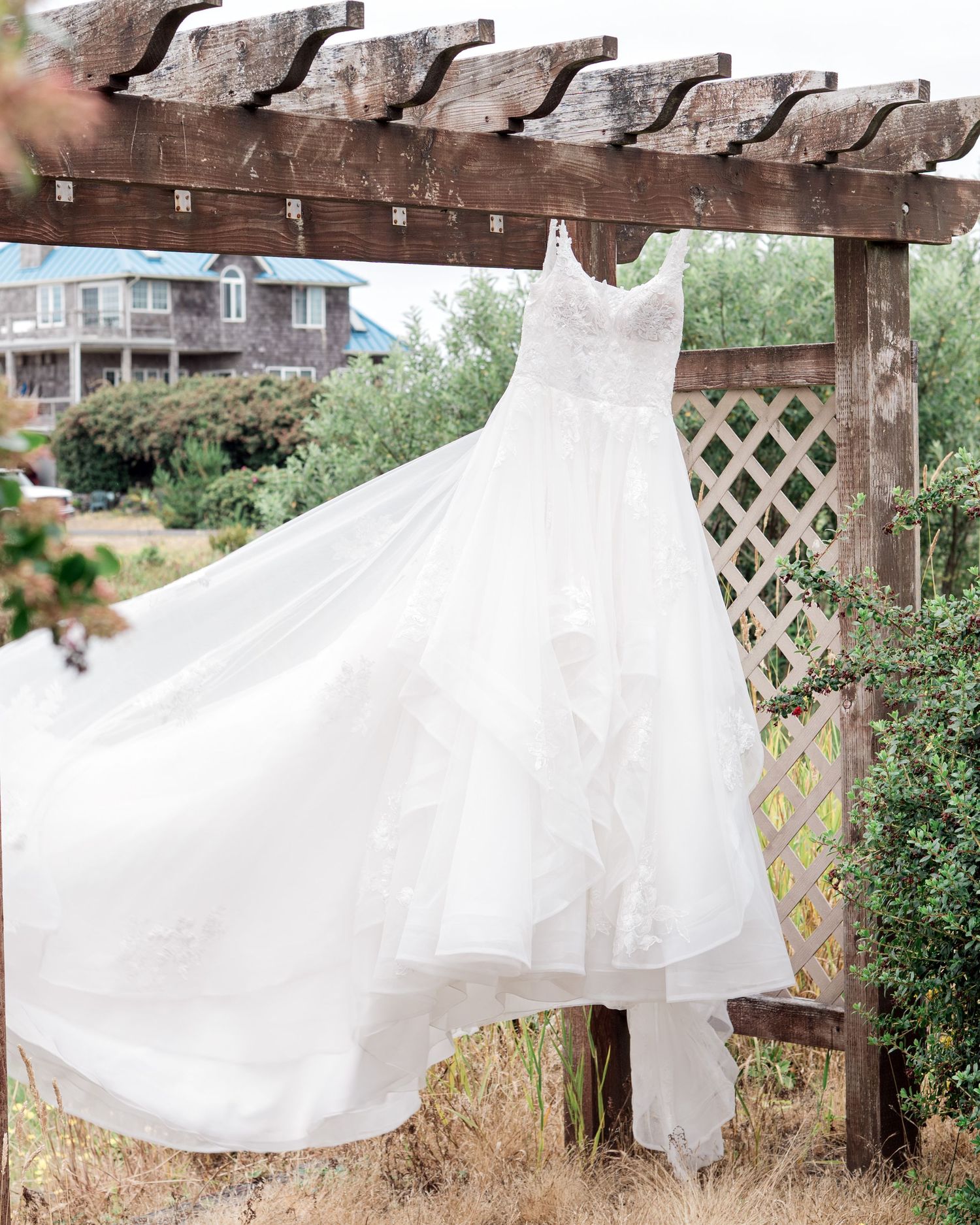 White wedding dresses hanging from a rustic wooden pergola with lattice details.