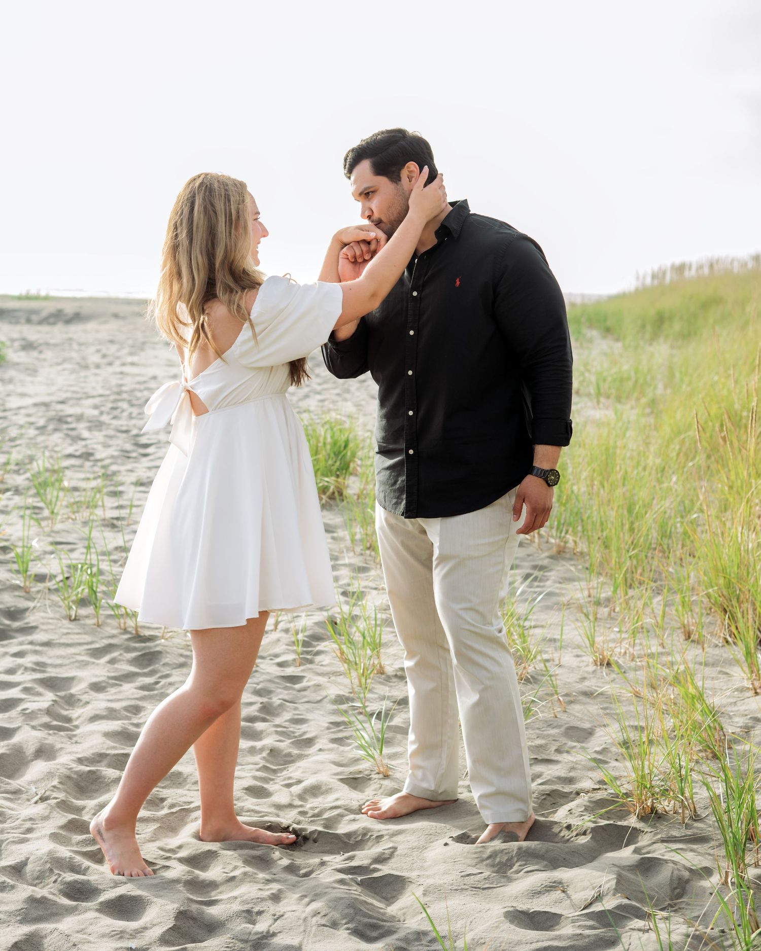 A romantic moment captured on a sandy beach with tall grass in the background.