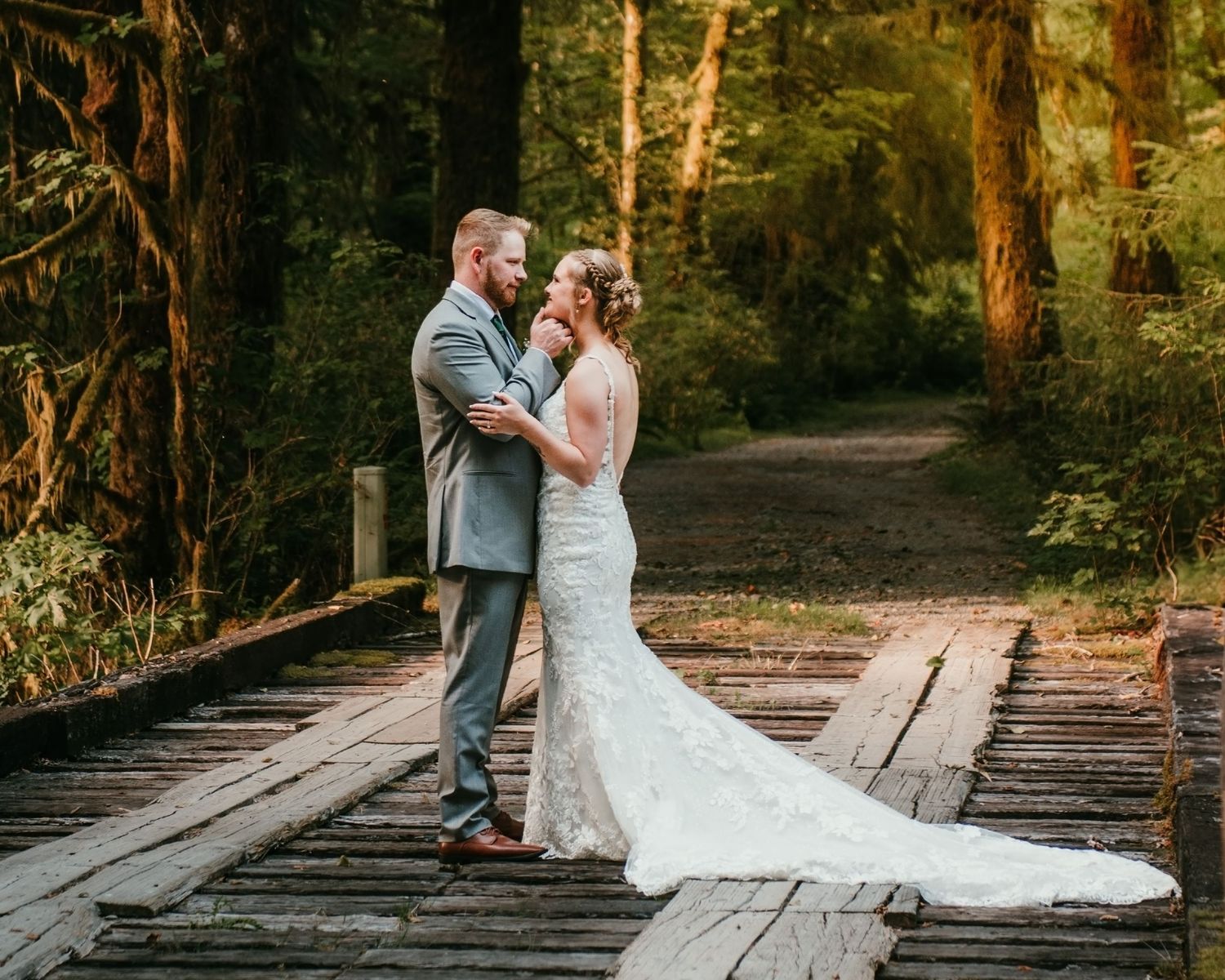 A romantic wedding portrait on a rustic wooden bridge in a sunlit forest.