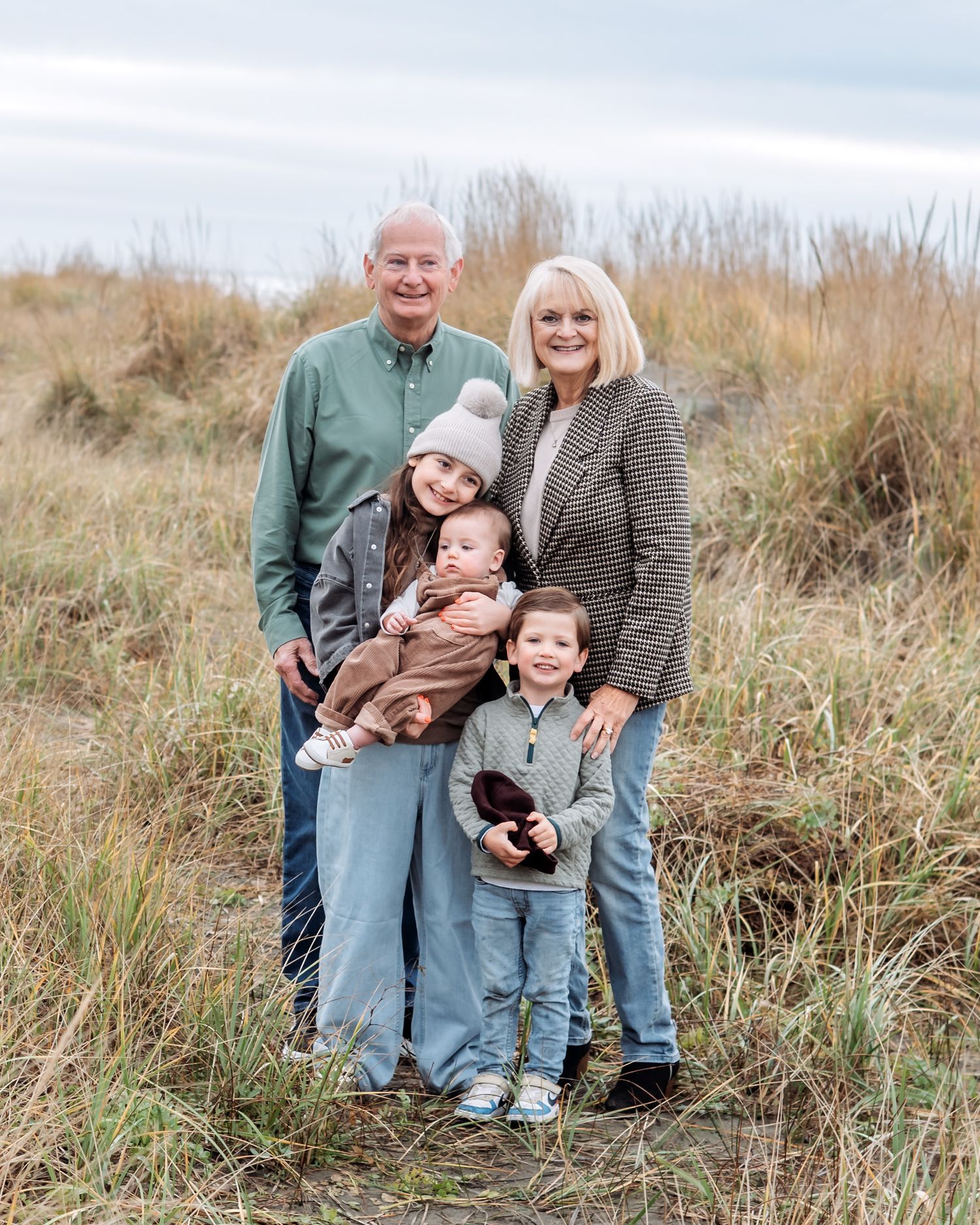 Grandparents posing outdoors with three grandchildren in a grassy field during a fall family portrait session.