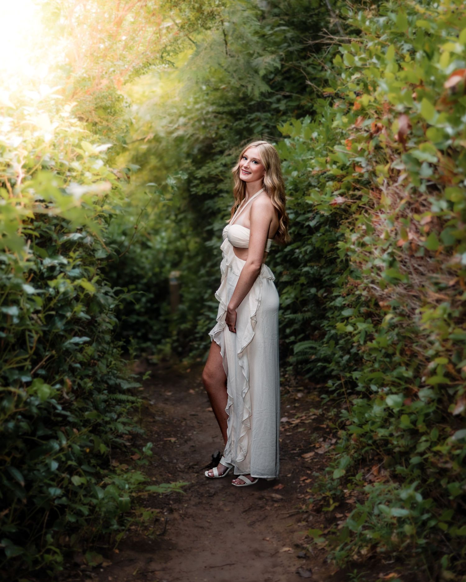 A dreamy portrait of a woman in white dress on a forest path at golden hour.