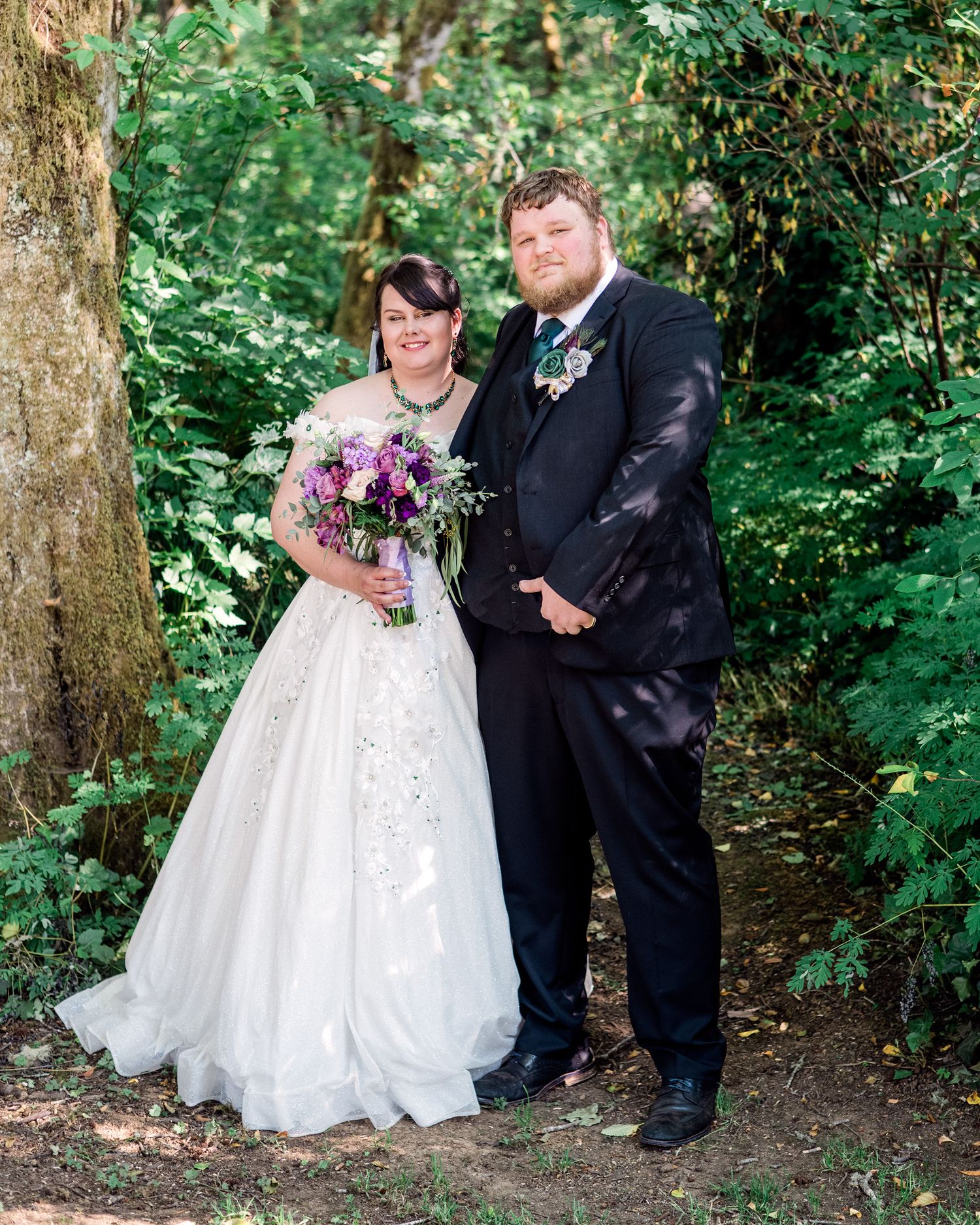 Wedding couple poses for romantic portraits under trees in a forest setting.