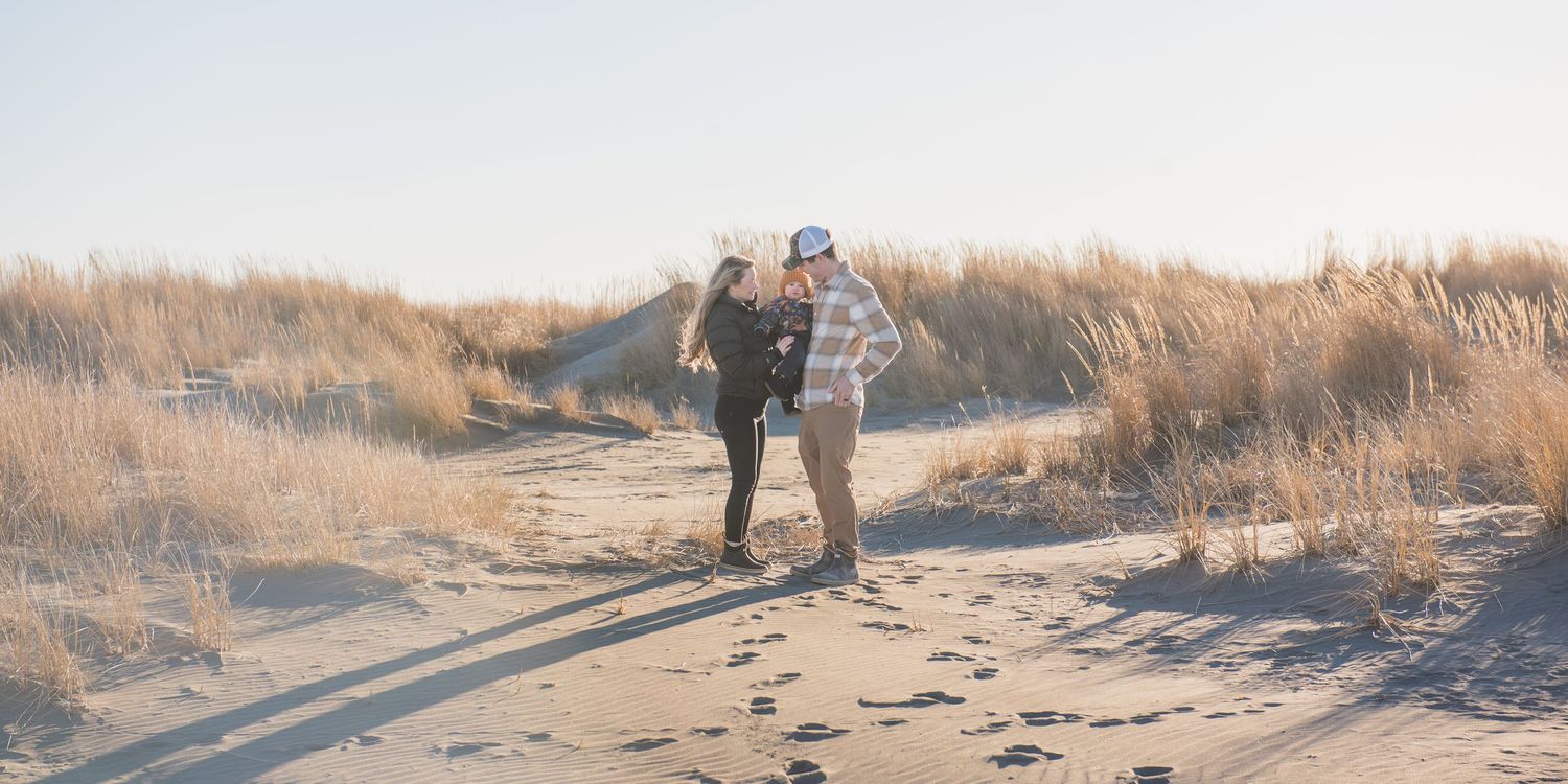 Couple walking hand in hand on a sandy beach path surrounded by golden dunes on a sunny day.