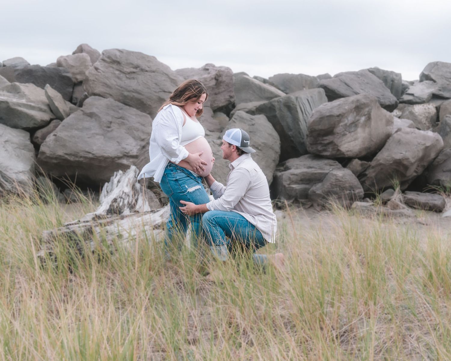 Couple shares intimate moment among coastal rocks and grass.