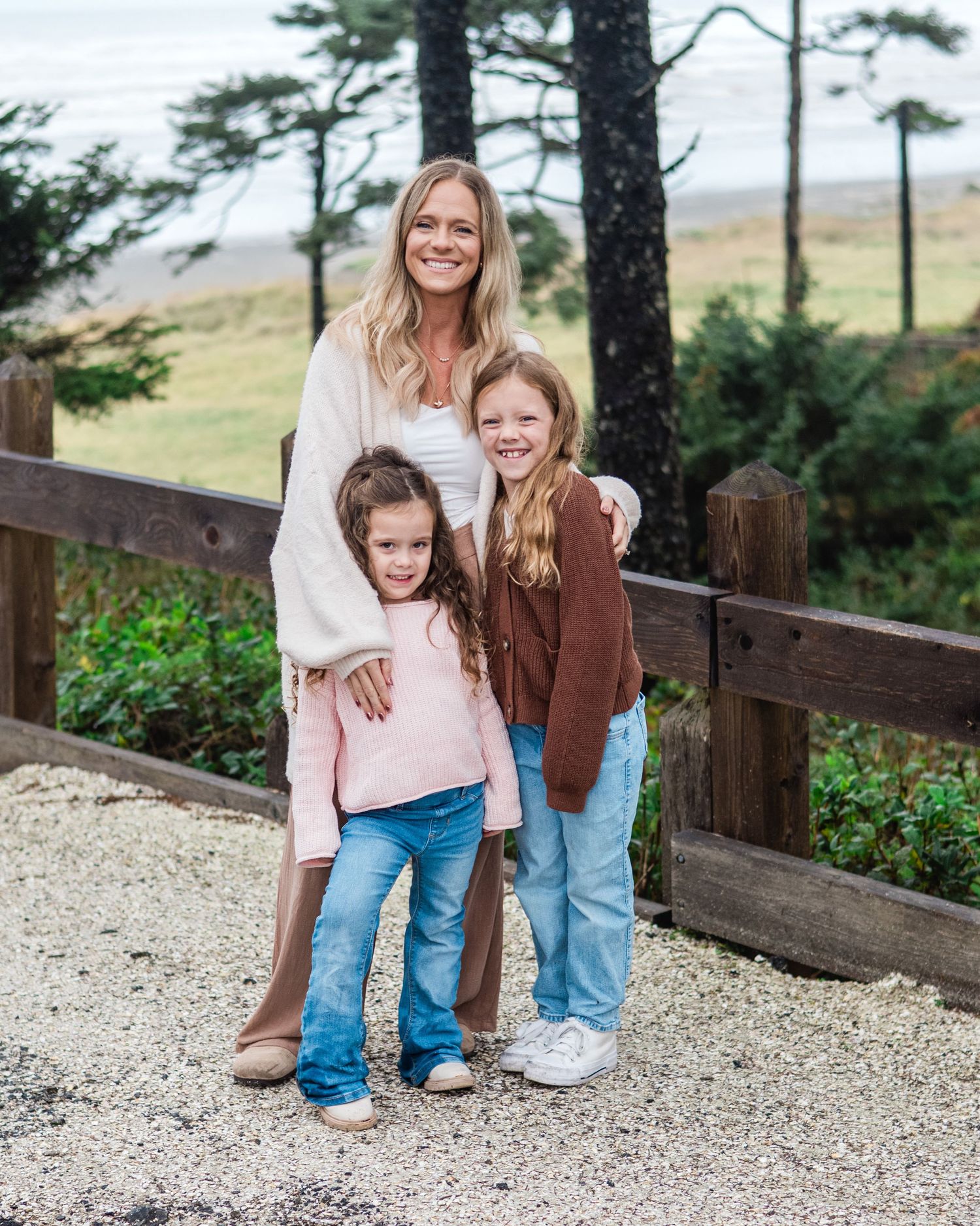 Family walks together on gravel path surrounded by evergreen trees.