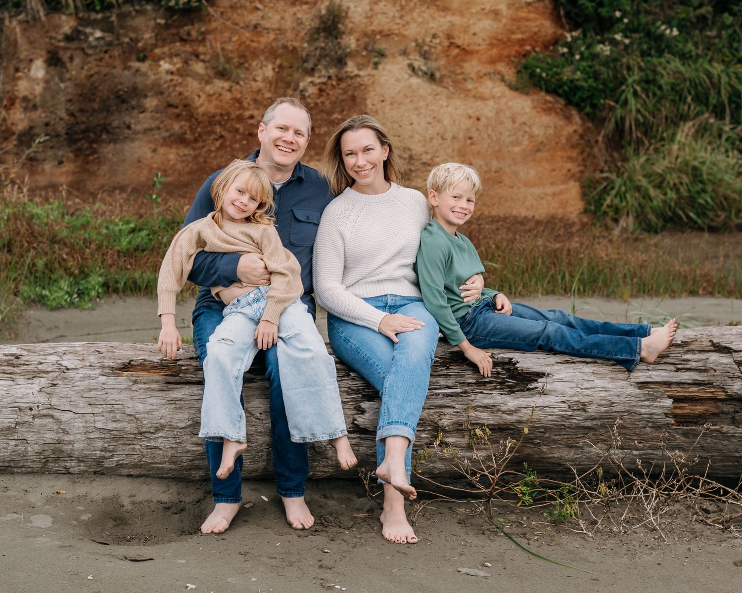 Casual family portrait session on a rustic log at the beach.