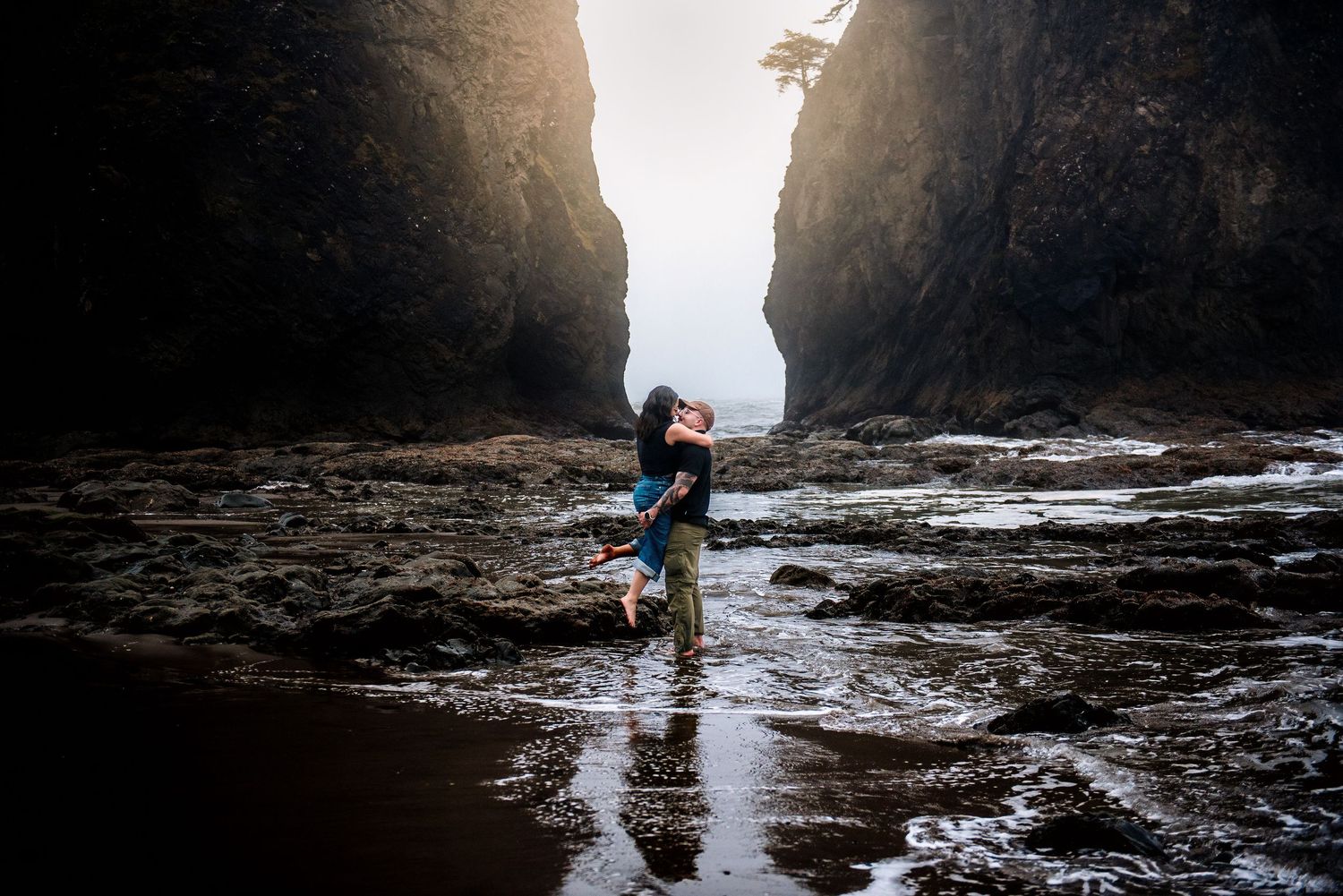 Couple embracing romantically between towering sea cliffs on a misty rocky beach.