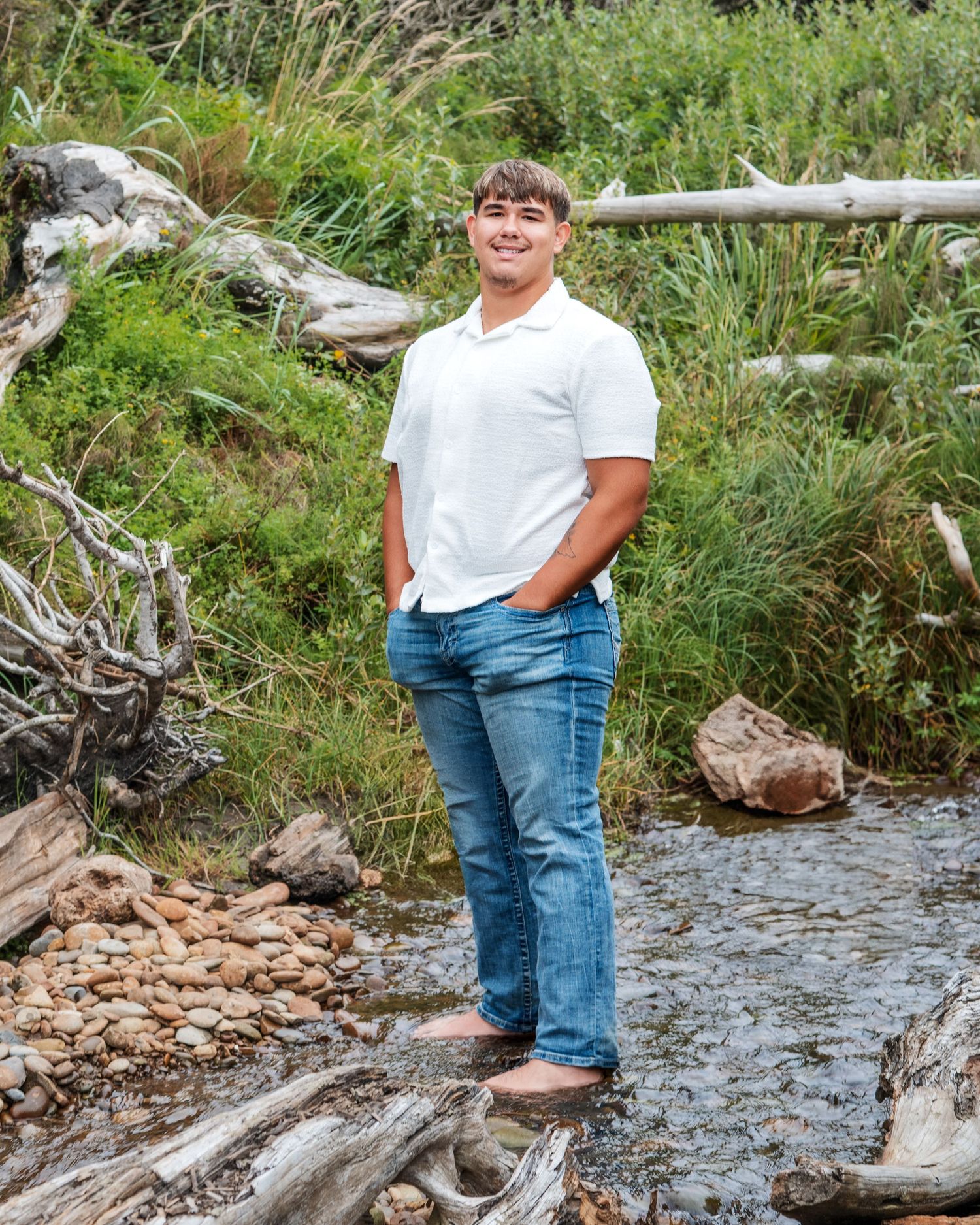 A casual portrait of someone standing on driftwood by a stream in nature.