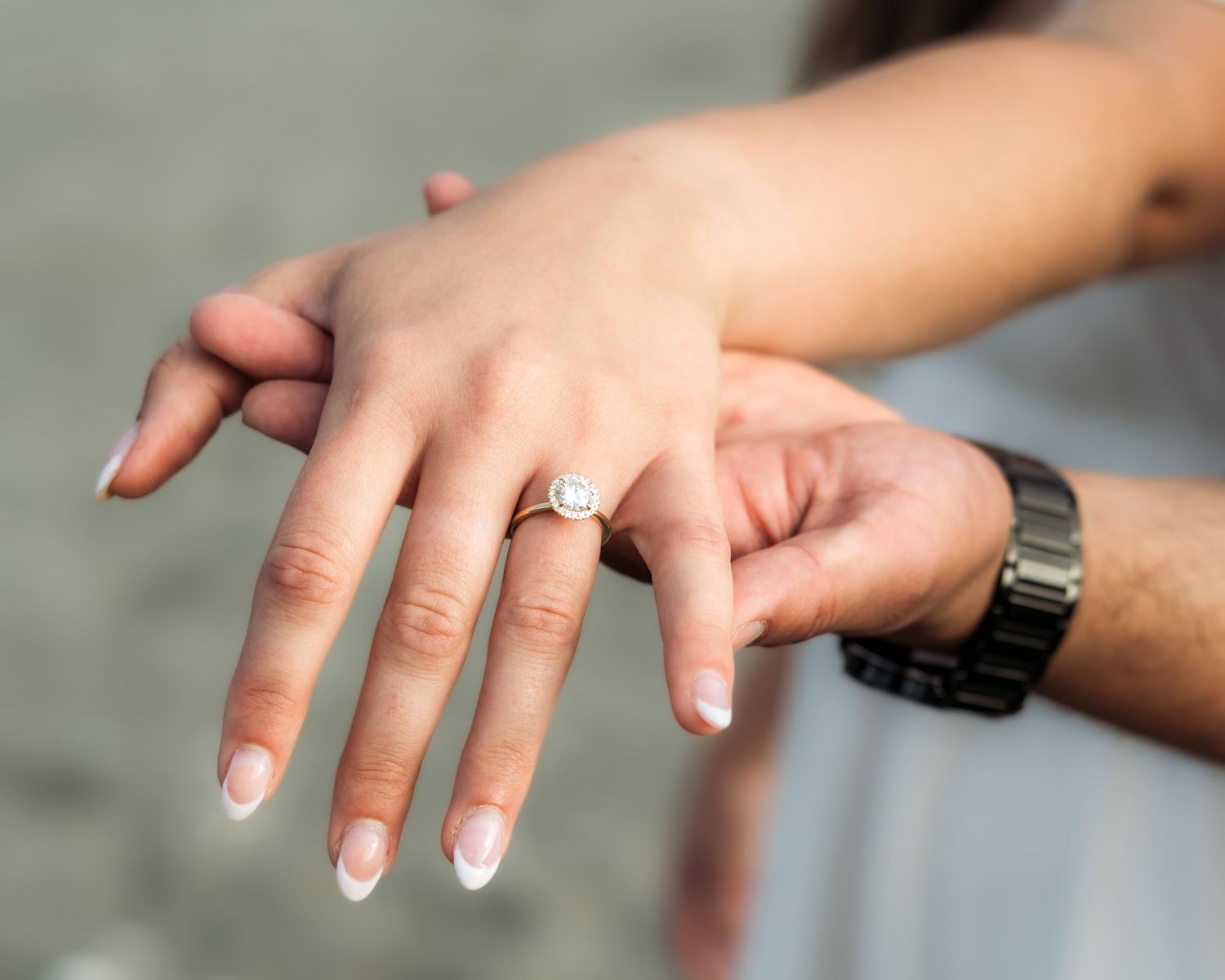 Close-up of hands showing off an engagement ring with a silver watch visible.