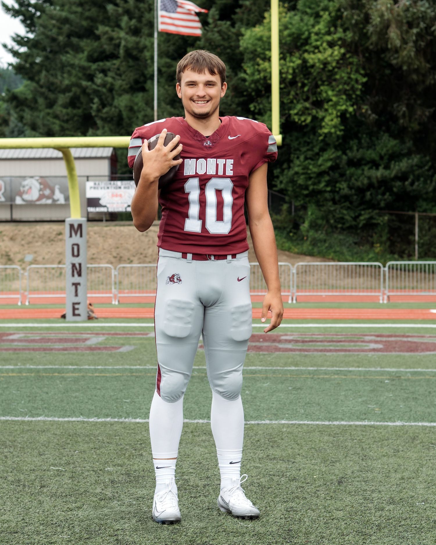 A football player poses in maroon and white uniform on a sports field.