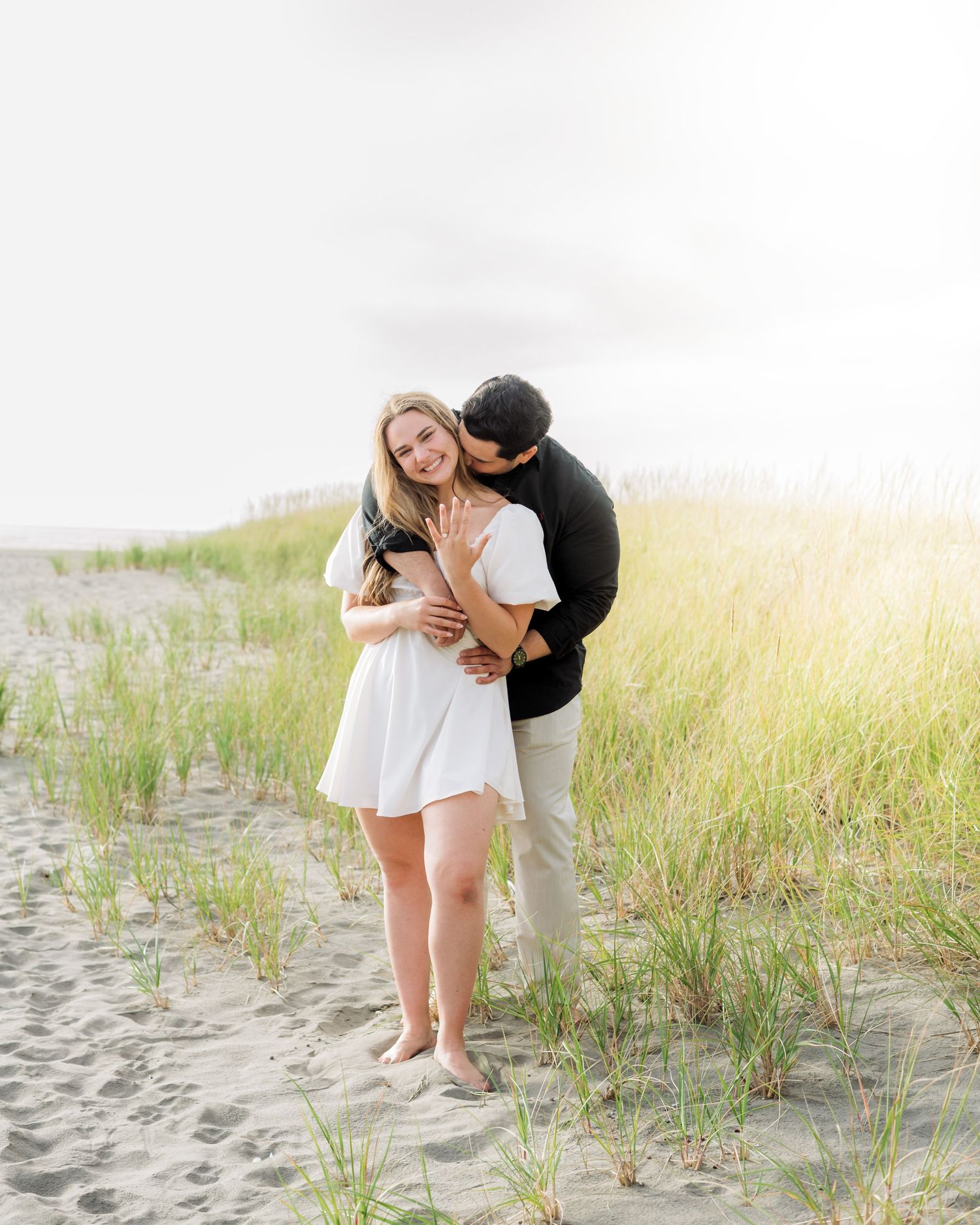 A tender moment shared between a couple on a beach with dune grass.