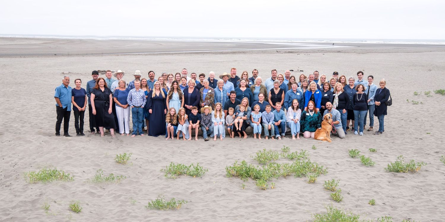 Large group of people gathered on a sandy beach landscape wearing blue and white casual attire for a group photo.