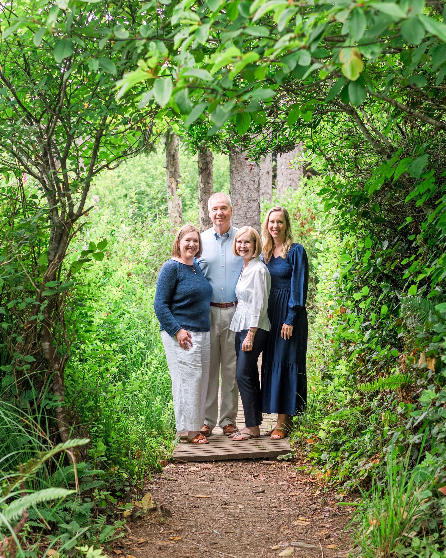 Family of four smiling together on a woodland path framed by lush green trees and foliage.